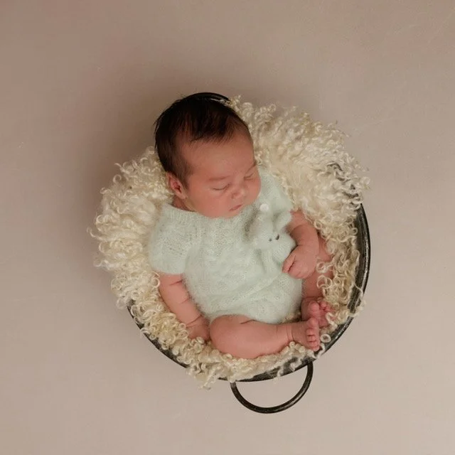 Photographed at Studio 5 by JK Photography, Carlisle, Cumbria. A new born baby sleeping in a black bowl surrounded by fluffy cream-colored material