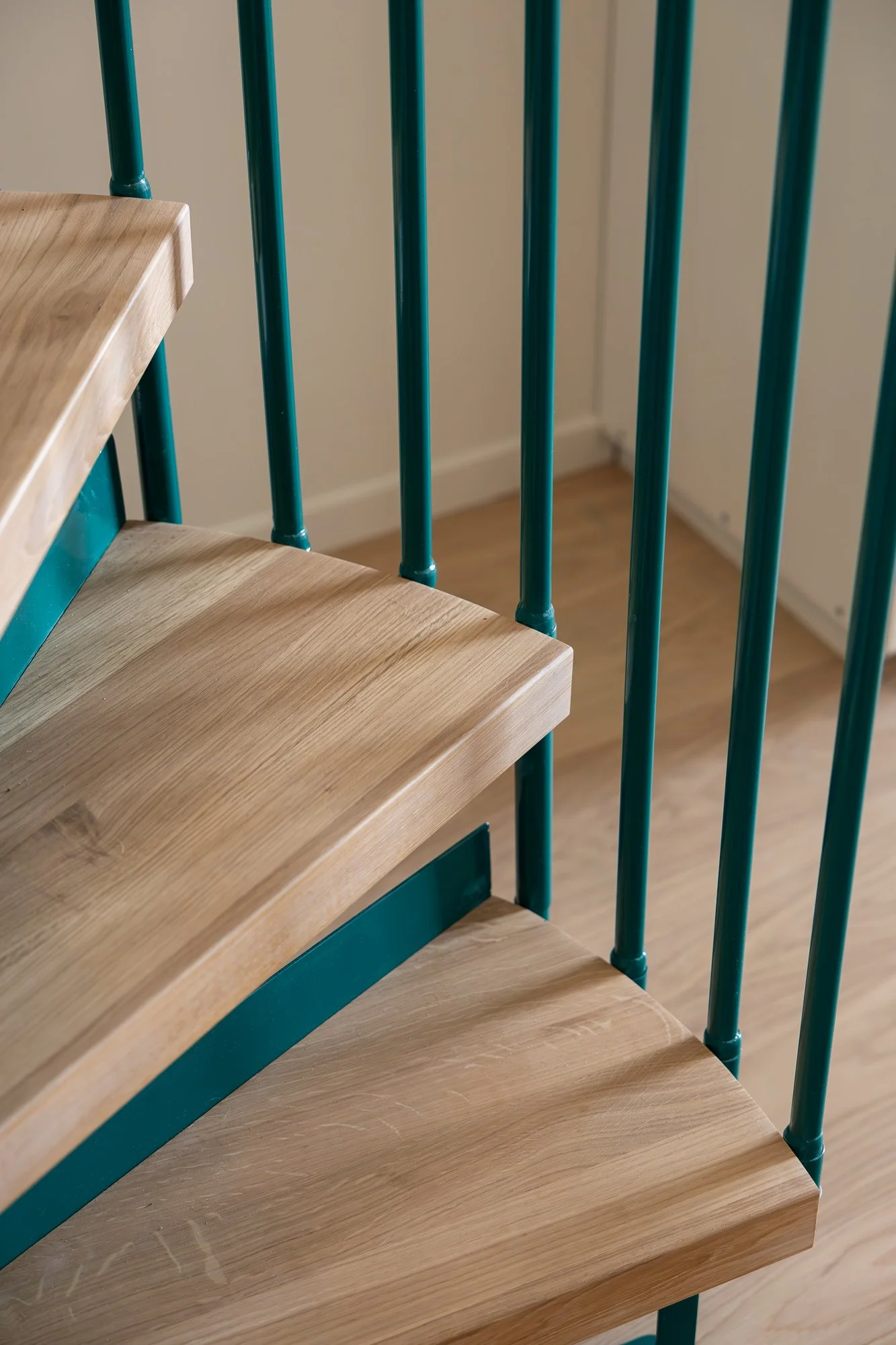 Close-up of a wooden staircase with teal-colored metal railings, showing the edge of three steps and part of the floor below.