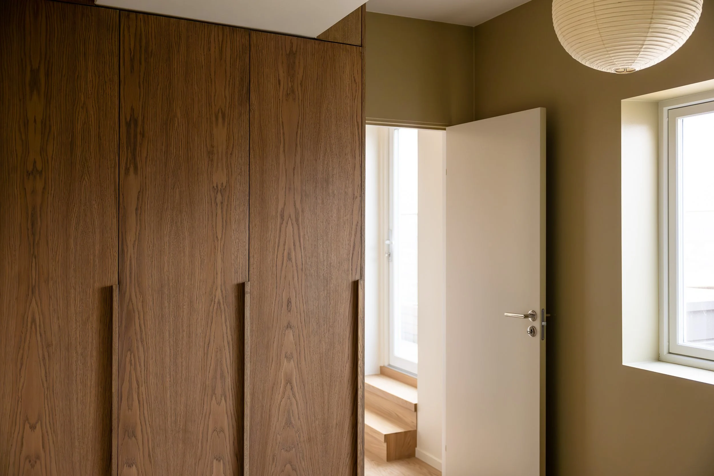 Room with wooden closet, open white door leading outside, window with natural light, paper lantern ceiling light