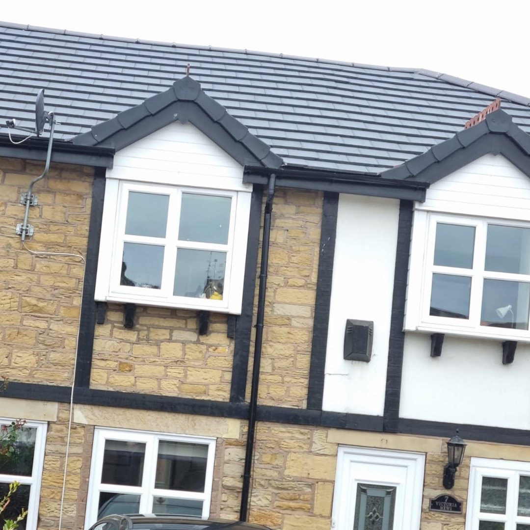 Close-up of a traditional brick house with white-framed windows, black trim, and a gray tiled roof.