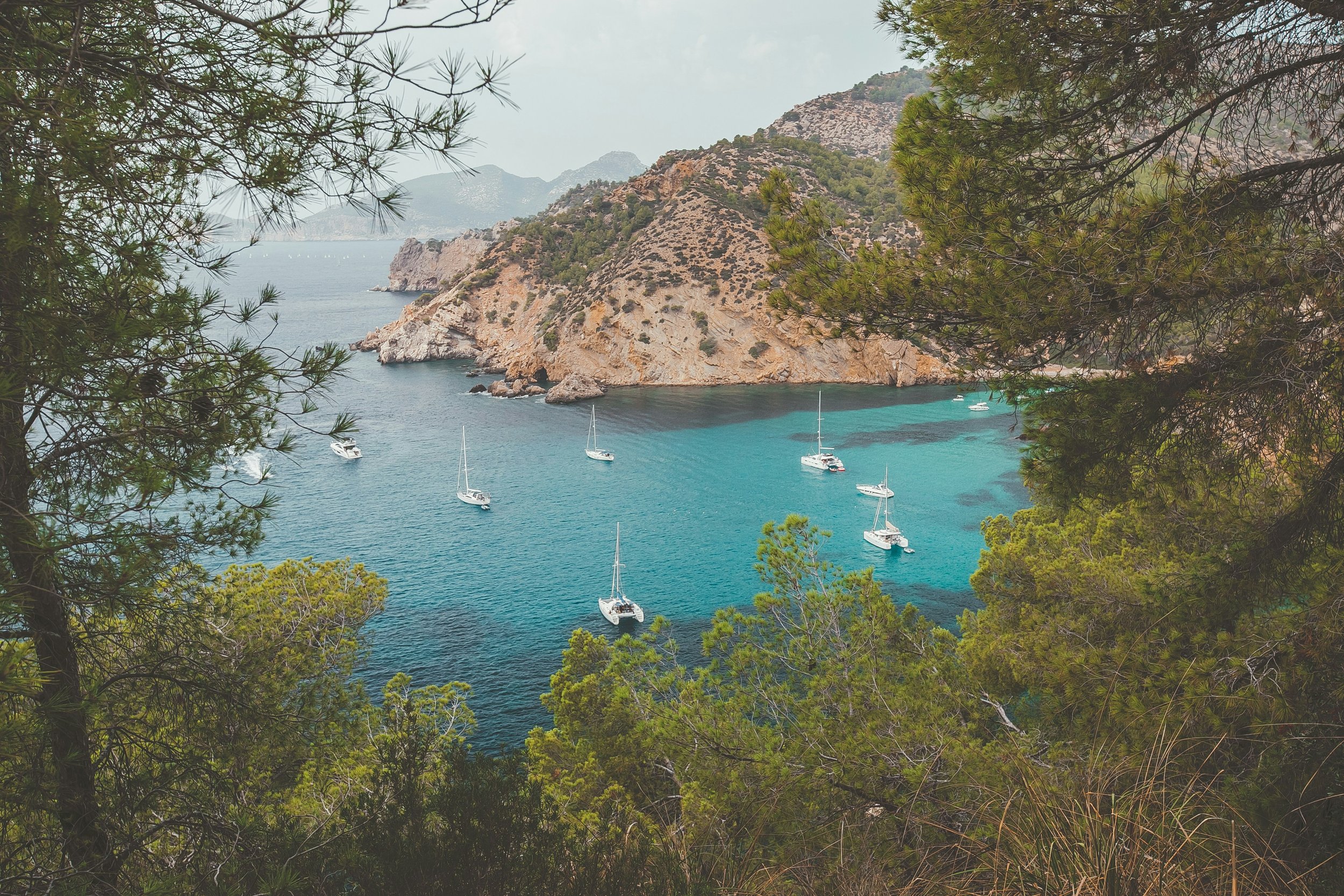 Paysage côtier avec des yachts dans une crique entourée de falaises rocheuses et de végétation verte.