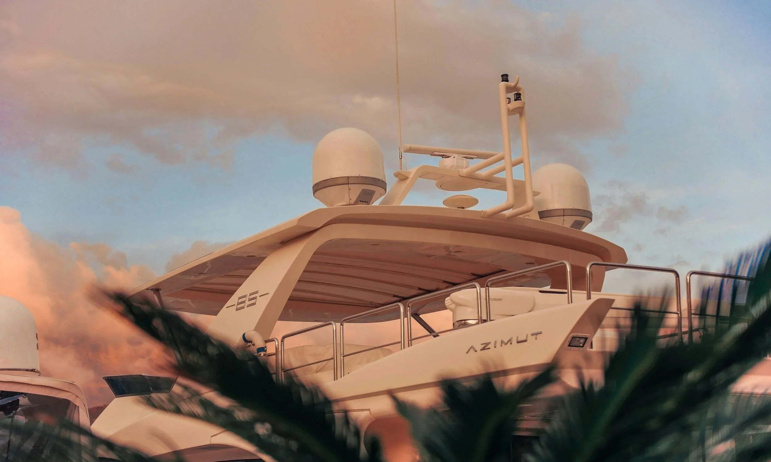 Un yacht blanc nommé AZIMUT, vue de face, avec une tour de transmission et des antennes, avec un ciel nuageux en arrière-plan.