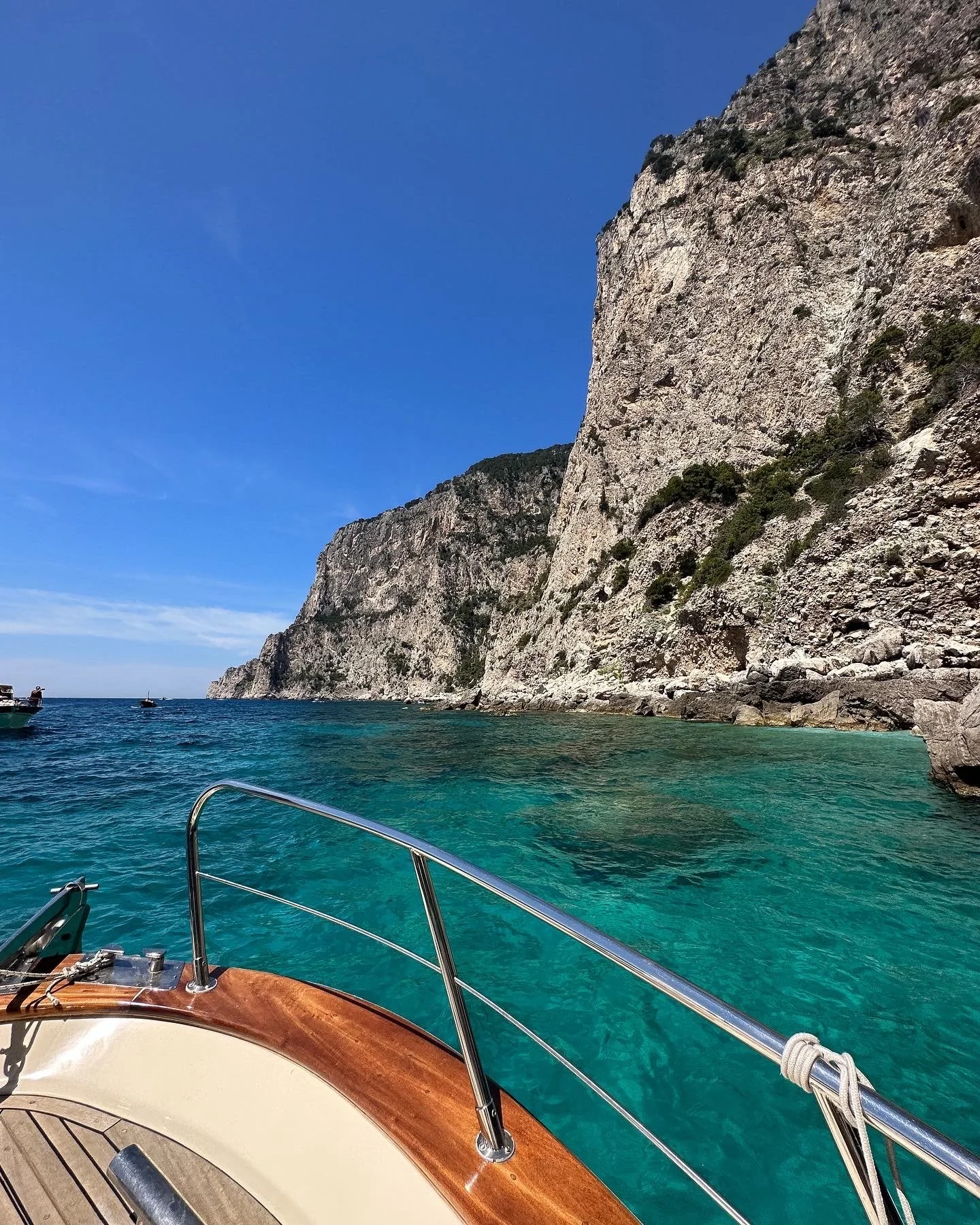 Vue d'une mer turquoise depuis un bateau, avec des falaises rocheuses escarpées au loin et un ciel bleu clair.