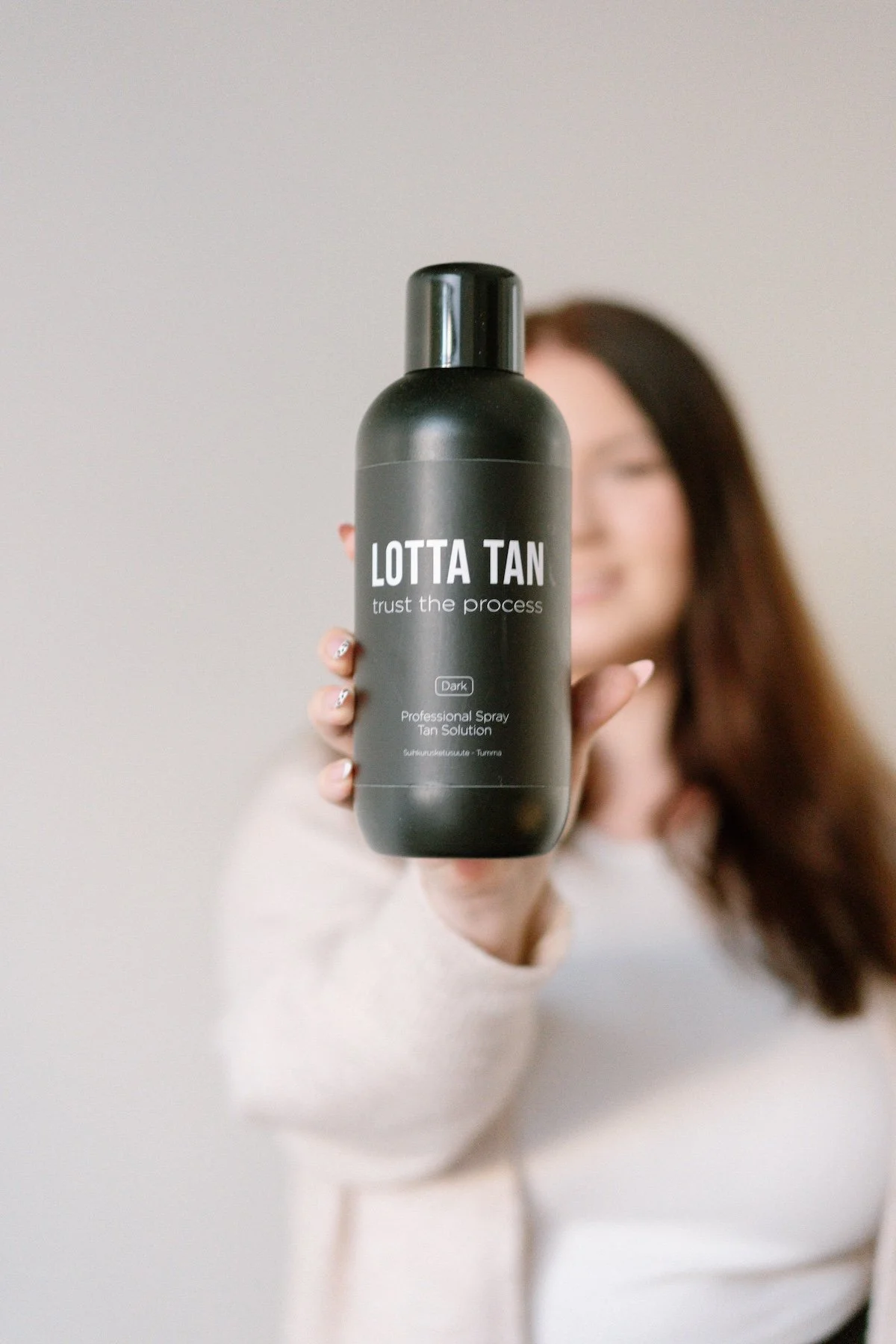 Suihkurusketuksen ammattilainen, joka pitää kädessään suihkurusketuspulloa.