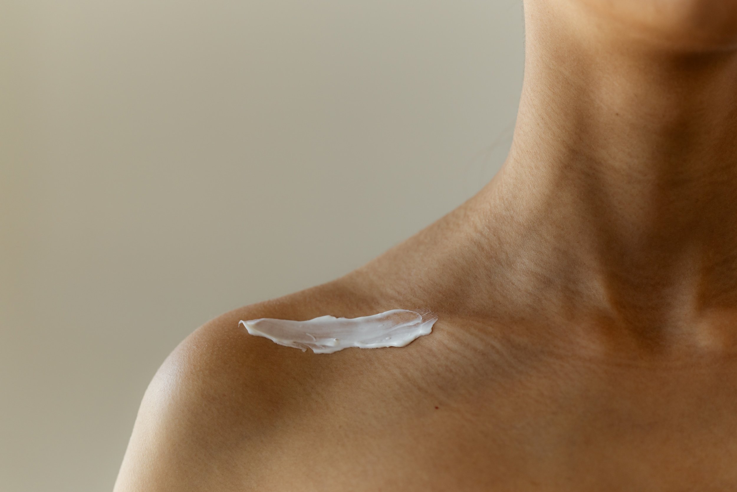 Ihmisen olkapää ja kosteusvoide ennen kosmetologin palveluja.