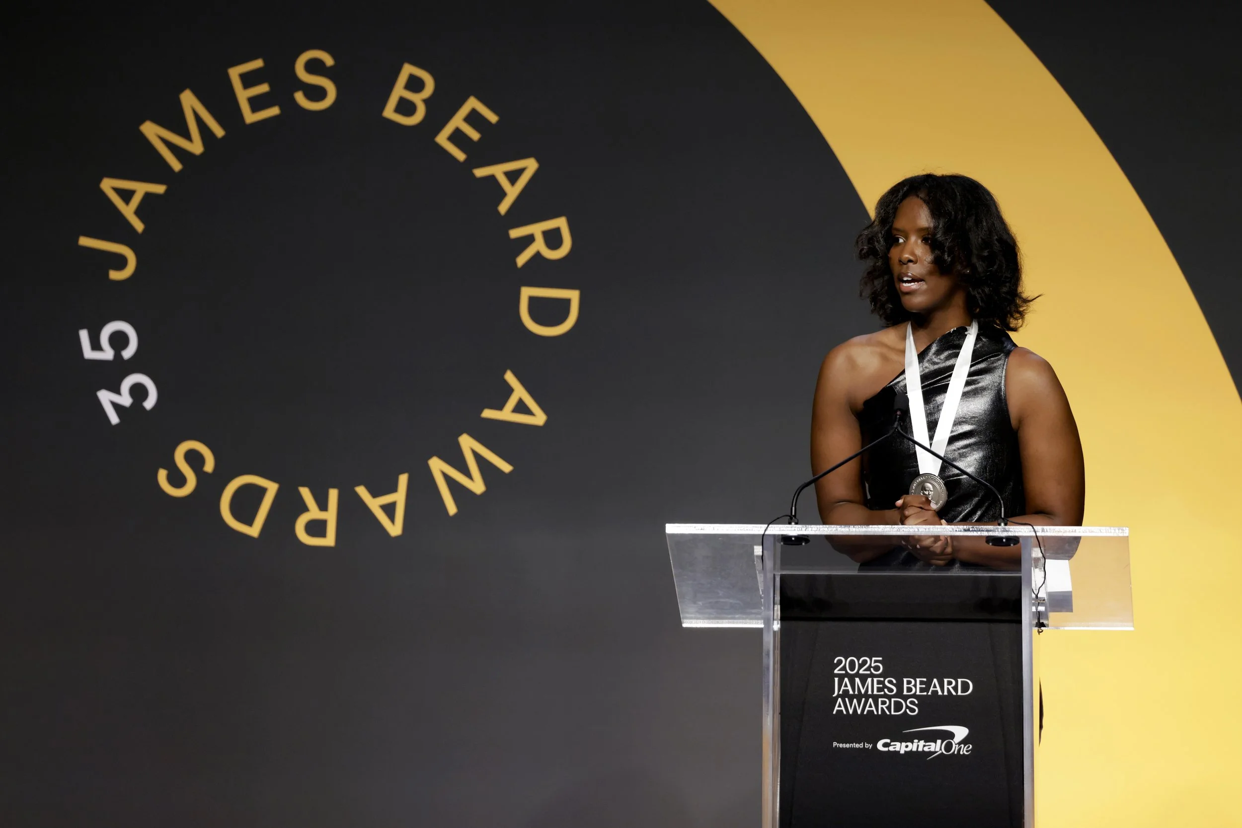 Anne-Marcelle Ngabirano speaking at a podium at the 2025 James Beard Media Awards wearing medal