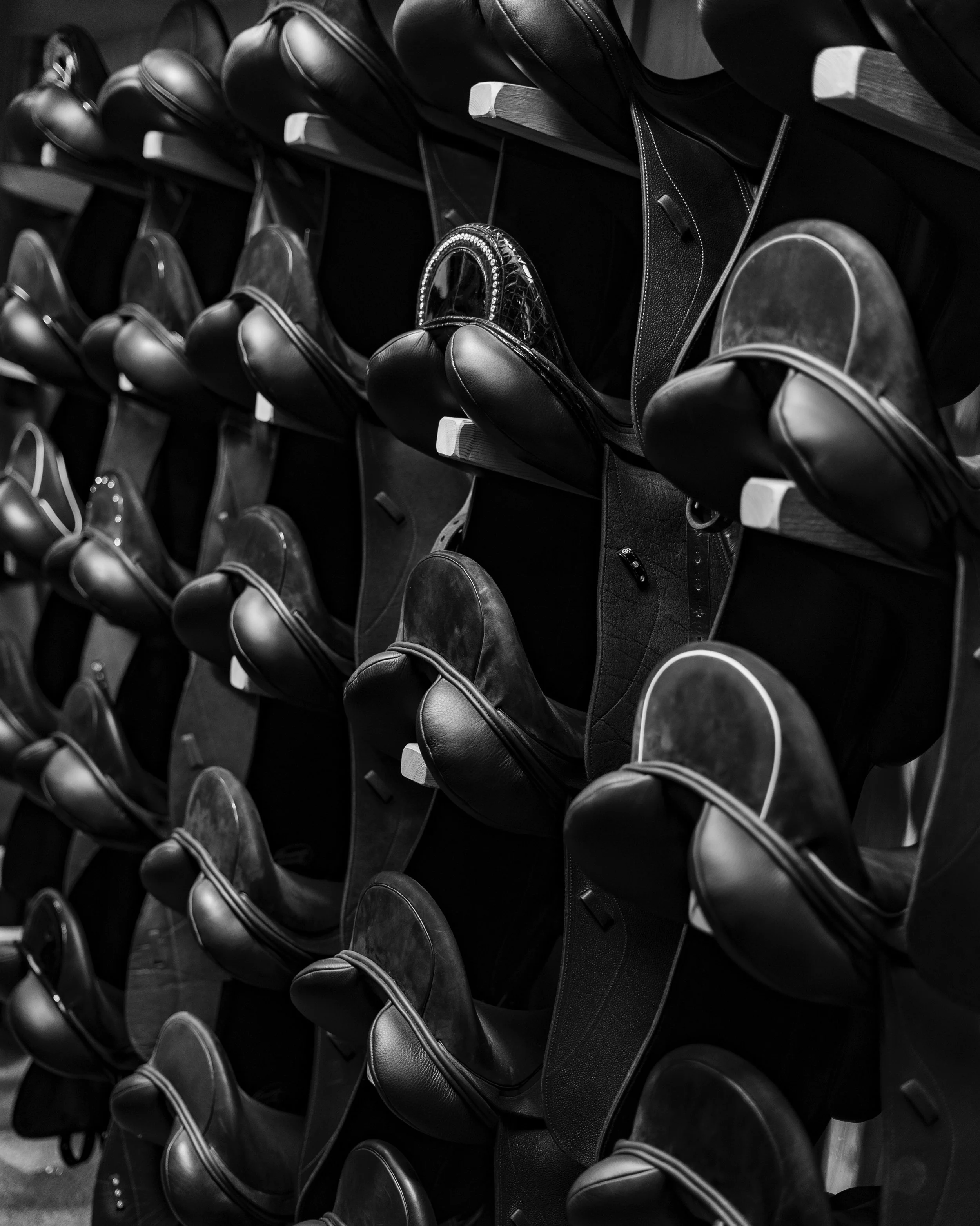 Detail of black leather Custom Saddlery saddles hanging. Some saddle have small extra details such as Swarovski