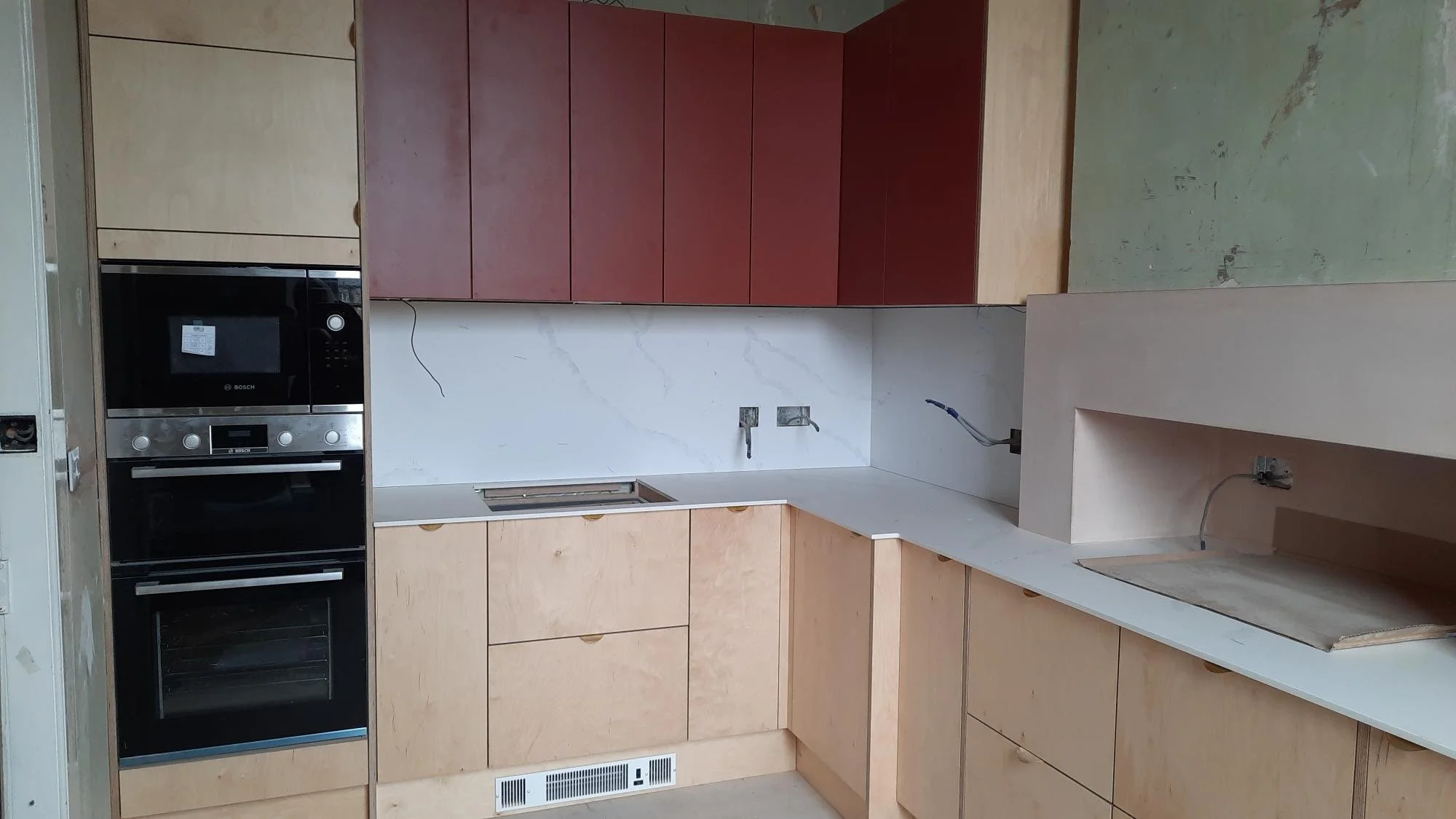 Kitchen with beige cabinets, black oven, and red upper cabinets. Countertop with built-in sink and open area for appliances, with some wiring visible on the wall.