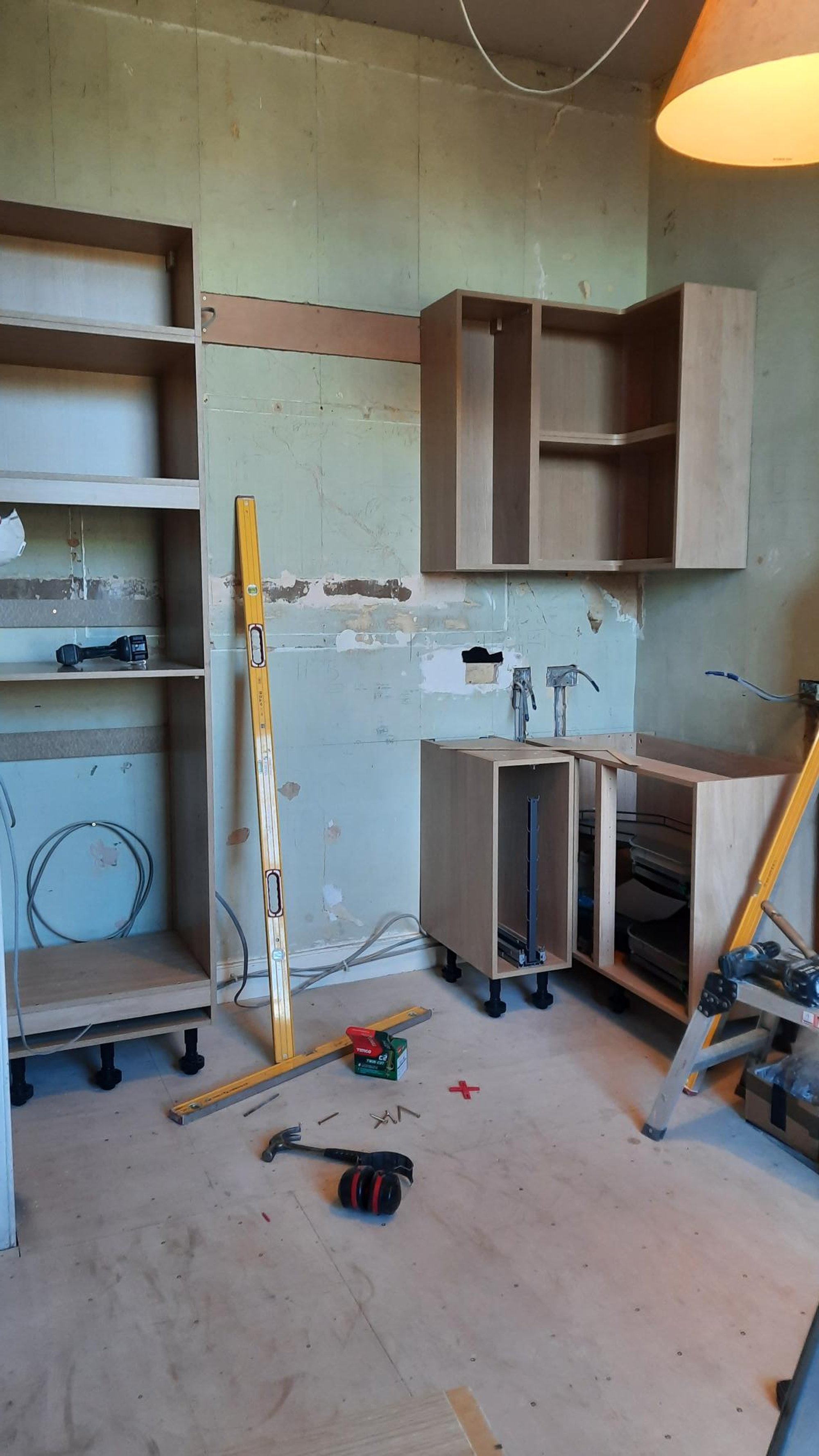 A kitchen under renovation with unfinished wooden cabinets, tools, and construction materials scattered on the floor.