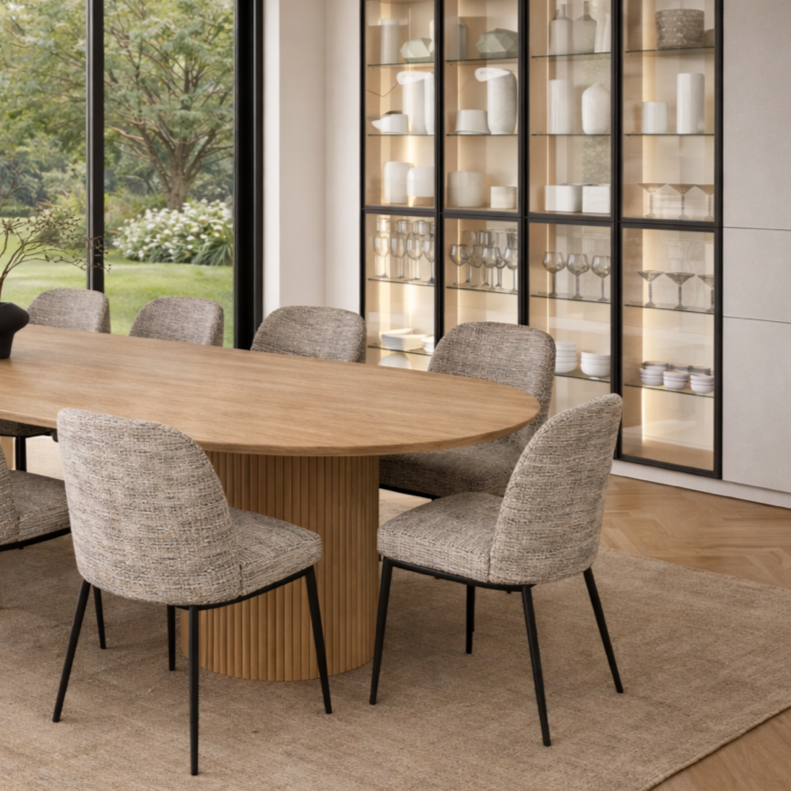 Modern dining room with a wooden oval table and six upholstered chairs; glass-fronted display cabinet with dinnerware and glassware; large window showing outdoor greenery.