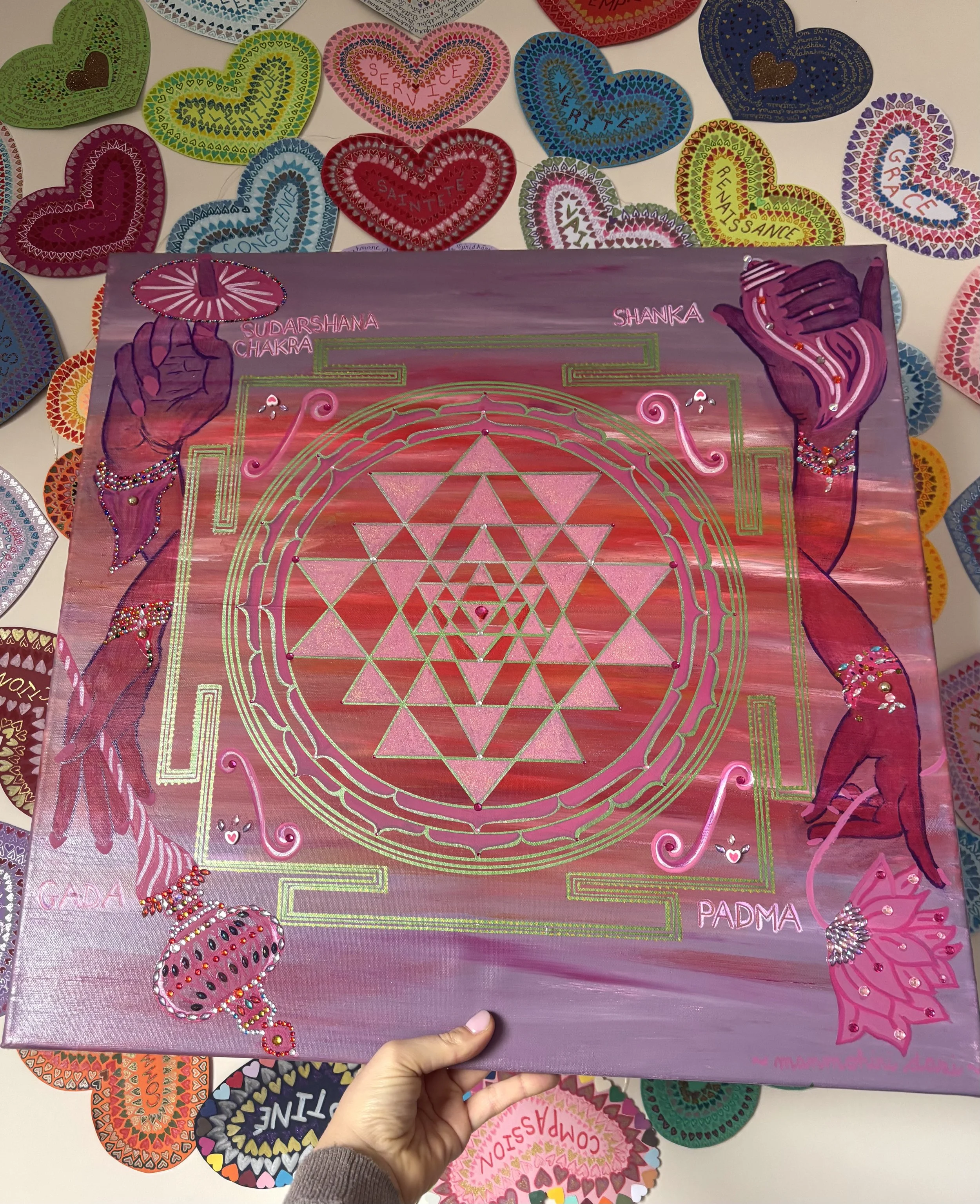 Une image d'un Sri yantra coloré, avec des diagrammes géométriques complexes et des illustrations de mains de Vishnu, entouré de cœurs en papier colorés avec des mots en français comme 'SERVICE', 'CONSCIENCE', 'GRACE', 'RENAISSANCE', et autres.