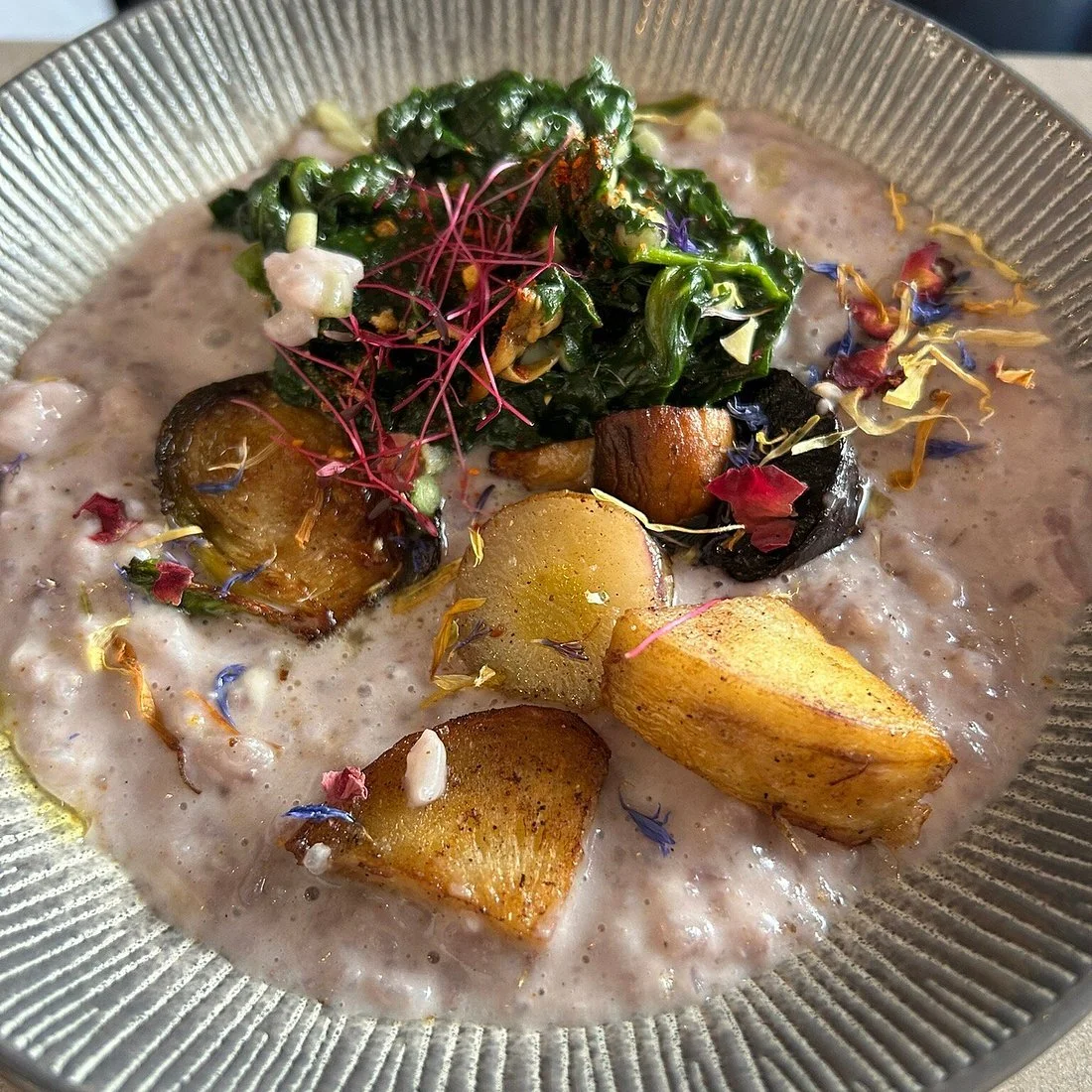 Le plat contient des pommes de terre rôties, des feuilles vertes sautées, des fleurs comestibles et une sauce crémeuse