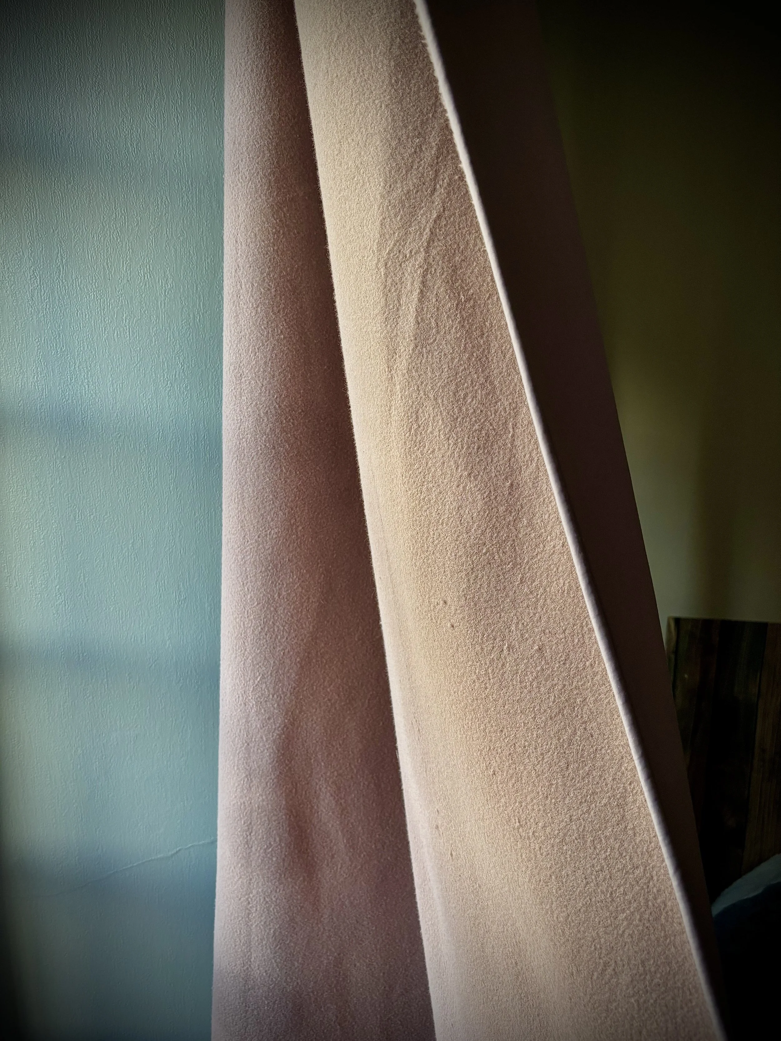 Des rideaux ou voilage en tissu léger, beige et rose, suspendus devant une fenêtre, avec une lumière naturelle passant à travers.