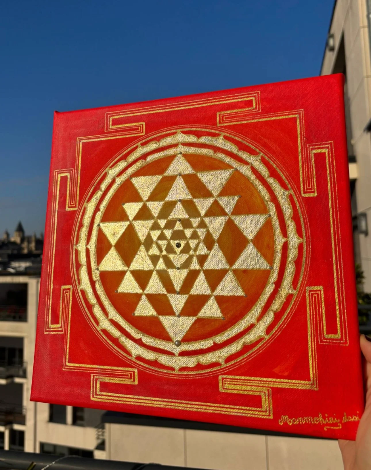 Sri Yantra Une peinture rouge et or représentant une géométrie sacrée avec un cercle central entouré de triangles, et un fond bleu clair.