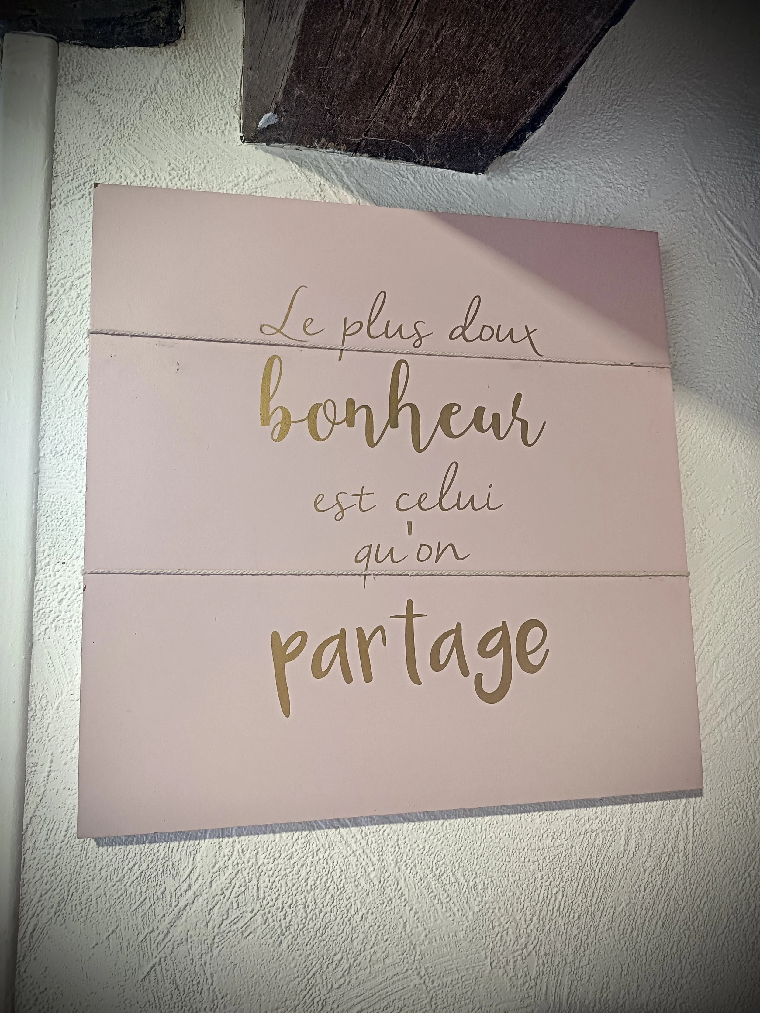 Une affiche rose clair avec un message en français écrit en lettres dorées : "Le plus doux bonheur est celui qu'on partage".