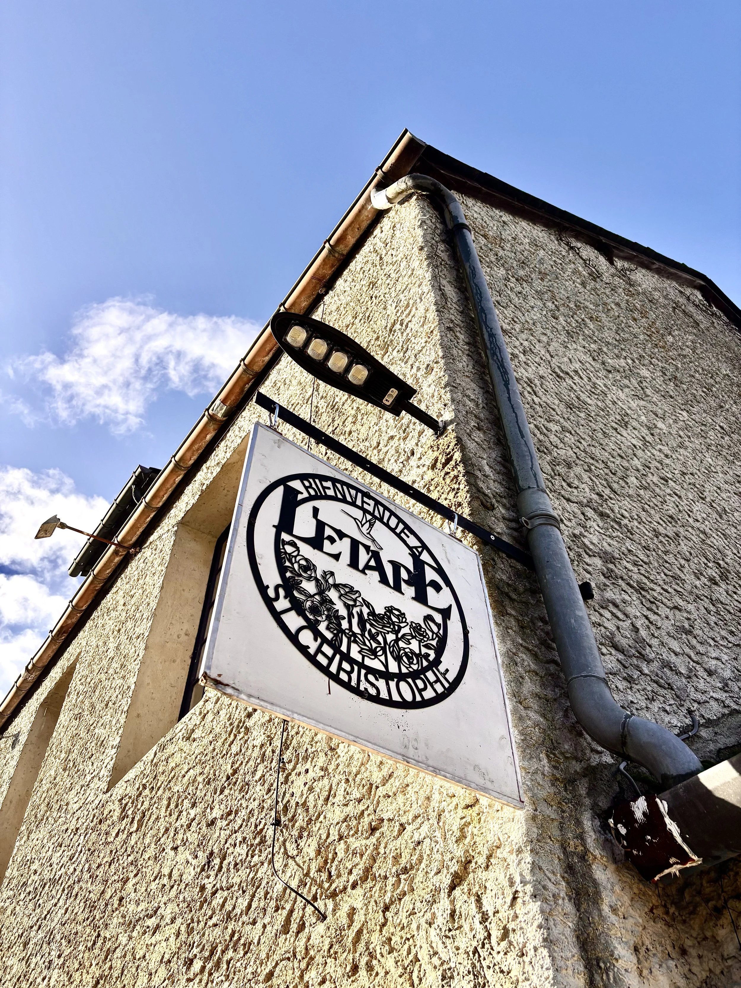 Panneau indiquant bienvenue en La State, un lieu ou un établissement, fixé à un bâtiment en pierre avec un éclairage en LED au-dessus.