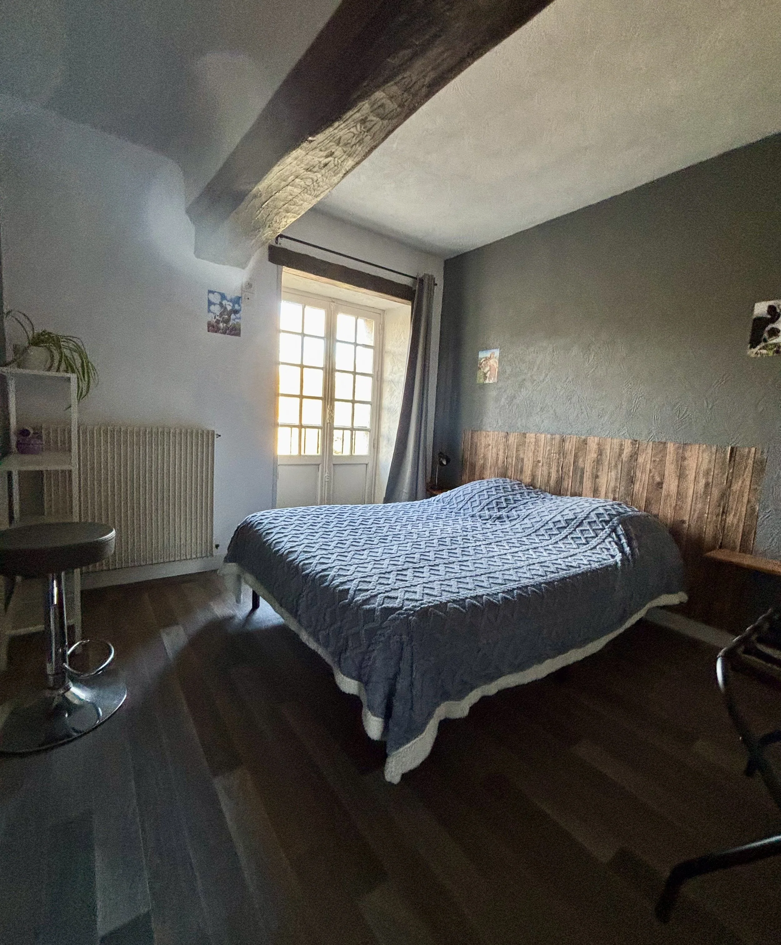 Chambre à coucher avec lit, tête de lit en bois, fenêtre avec lumière naturelle, mur gris, décorations murales, sol en bois, mobilier minimaliste.