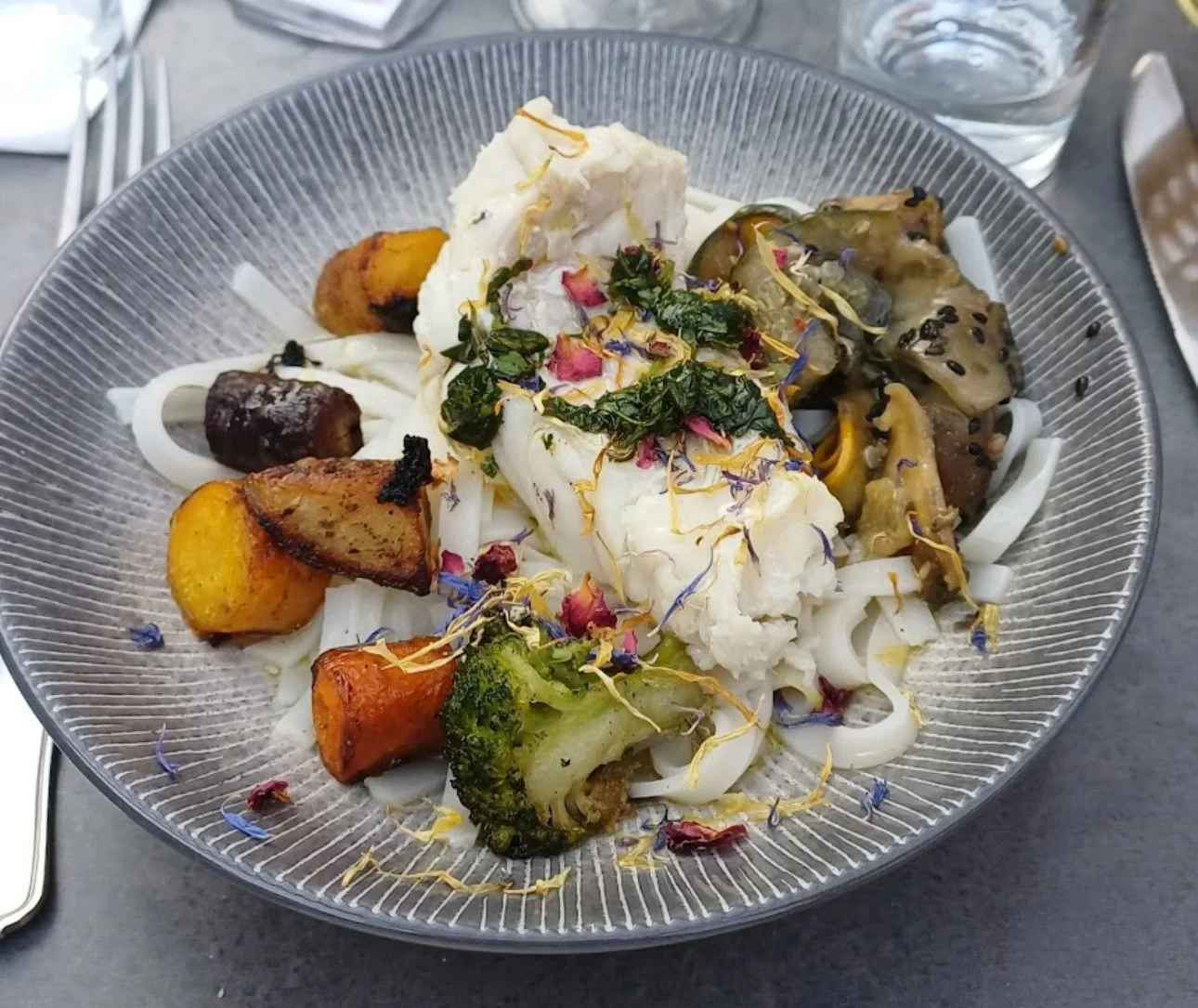 Plat de cuisine végétarienne avec des légumes grillés, des feuilles vertes, des fleurs comestibles et des pâtes