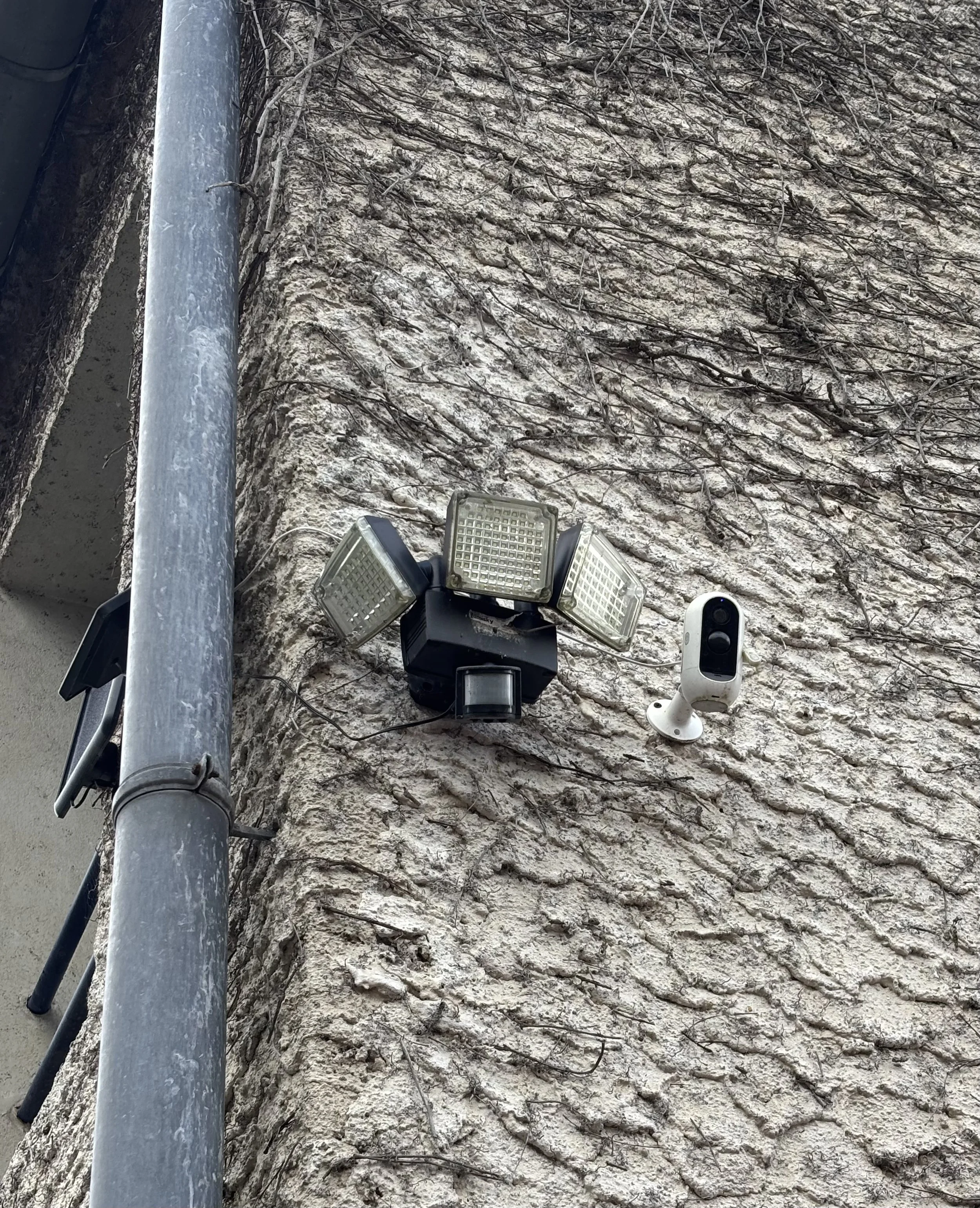Caméra de surveillance et éclairage extérieur fixés à un mur en pierre.