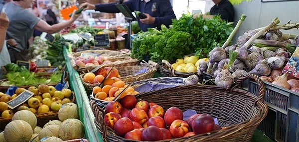 Légumes et fruits frais dans un marché, dont des pommes, des melons, de l'ail, des pêches, et des légumes verts.