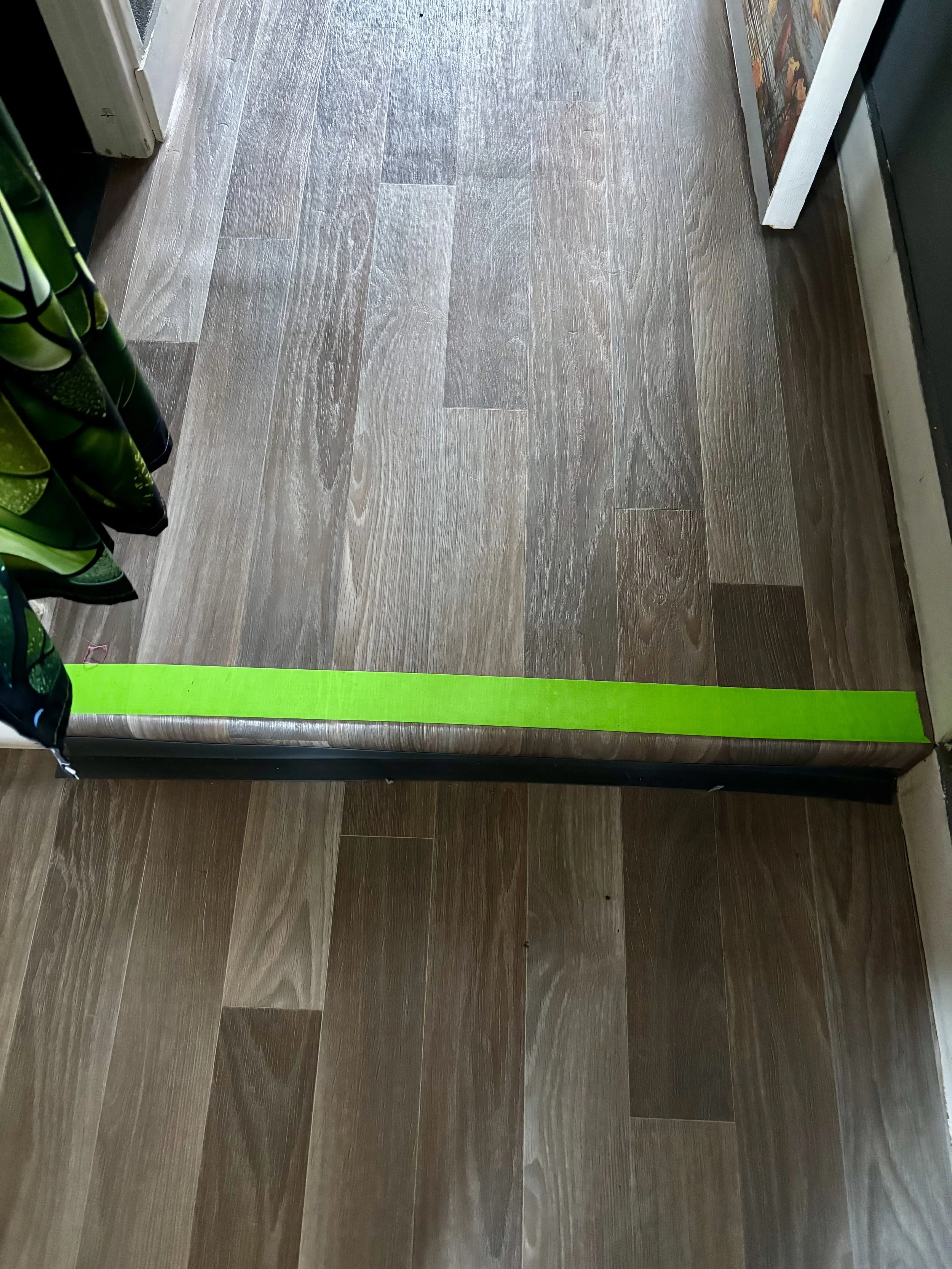 Un sol en bois avec une bande de ruban adhésif jaune fluo posée horizontalement sur le sol.