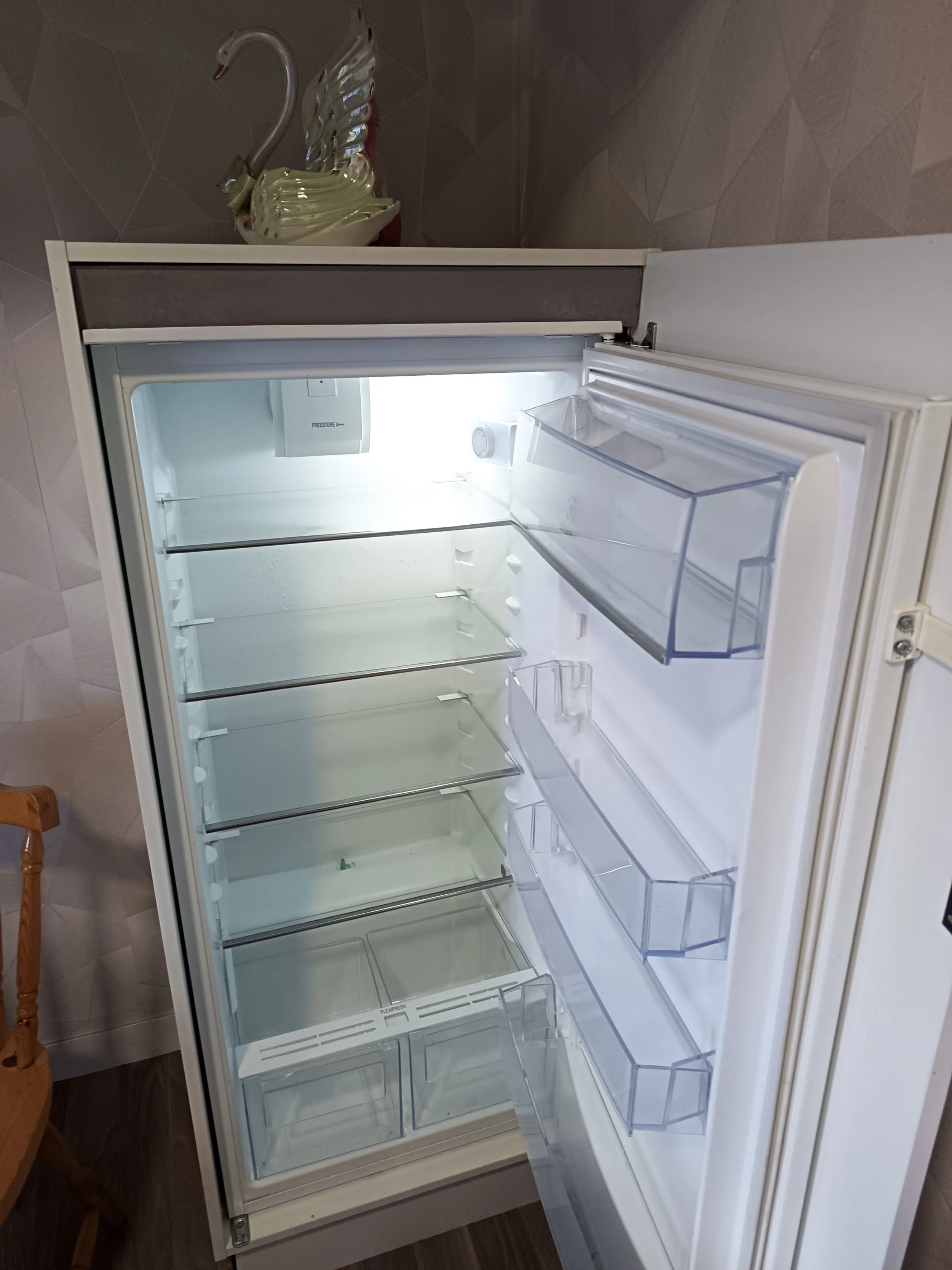 Réfrigérateur vide ouvert dans une pièce, avec des étagères et des compartiments transparents.