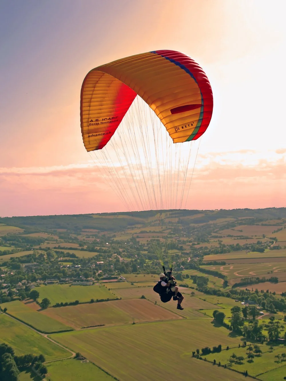 Une personne faisant du parapente dans le ciel au coucher du soleil au-dessus d'une campagne verdoyante.