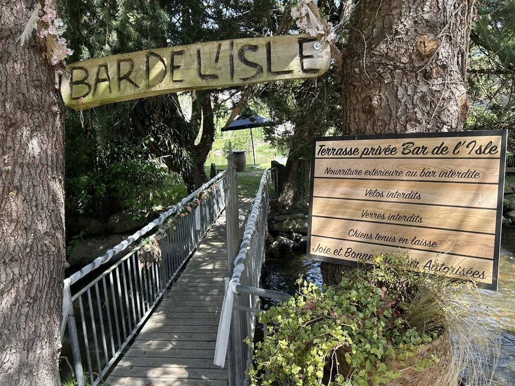 Un pont en bois menant à une terrasse privée entourée de végétation, avec des panneaux en bois indiquant les règles de l'endroit