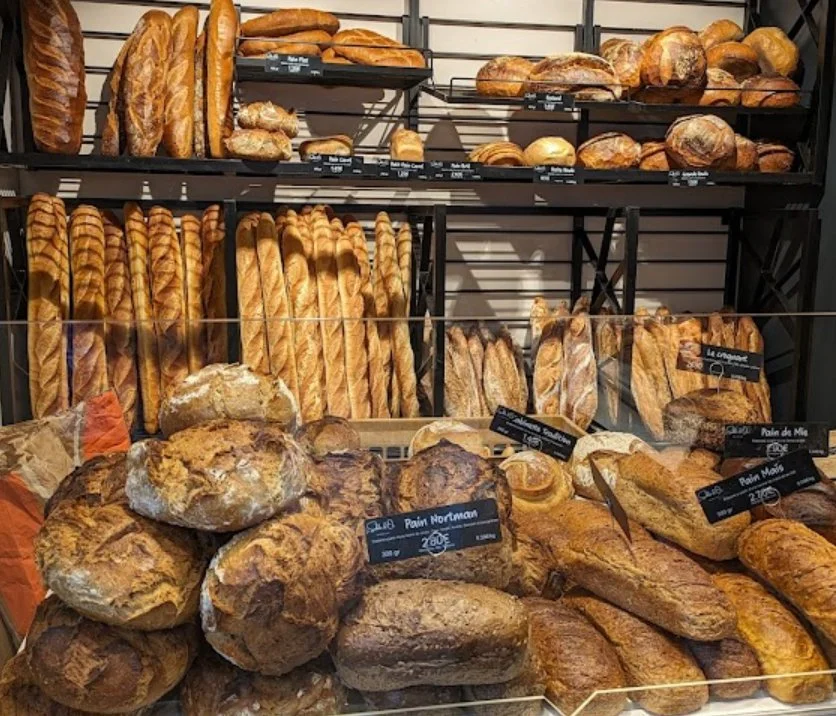 Différents types de pains, y compris des baguettes, des pains ronds, et des pains de campagne, exposés dans une boulangerie.