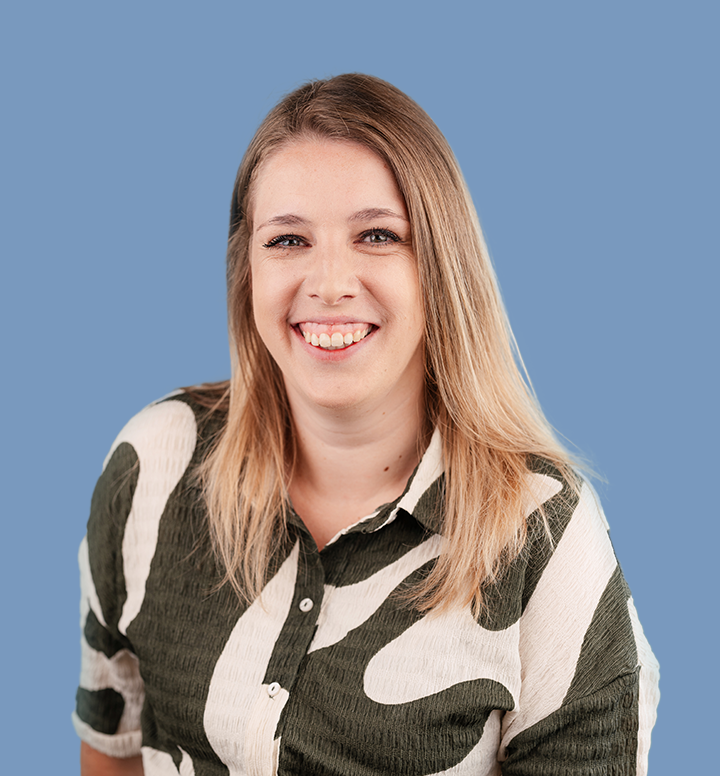 Portret van een lachende vrouw met lang blond haar die een zwart-wit gebreven blouse draagt, tegen een effen blauwe achtergrond.