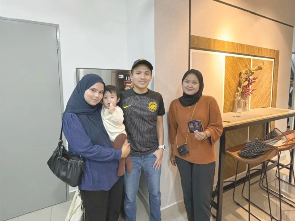 Four women and one young girl are standing and smiling in an indoor setting with modern decor. One woman is holding the girl, and two women are holding pamphlets or cards.