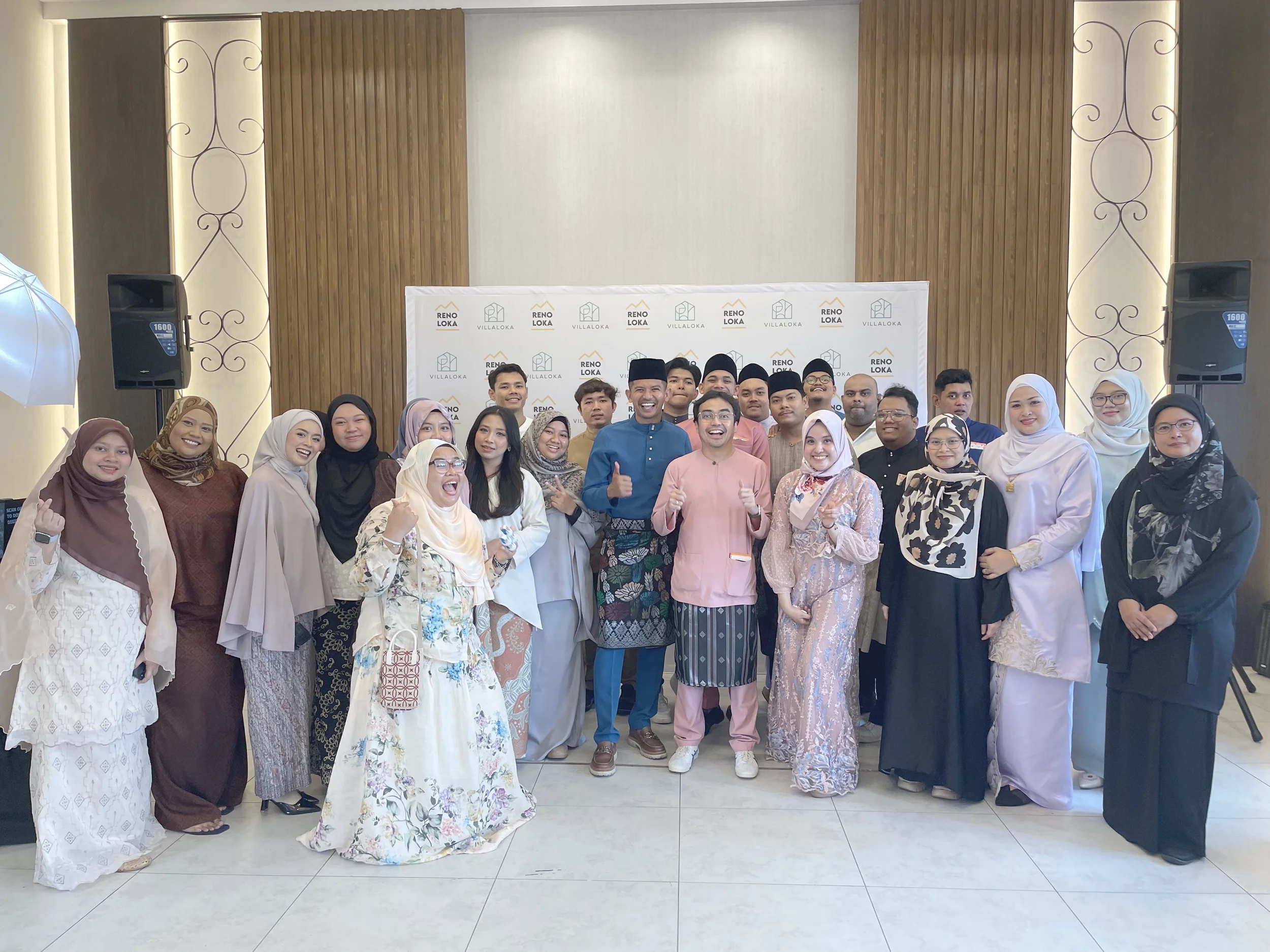 Group of diverse people smiling and posing for a photo in front of a backdrop with 'Reno Loka' and 'Villaloka' logos, at an indoor event or gathering.