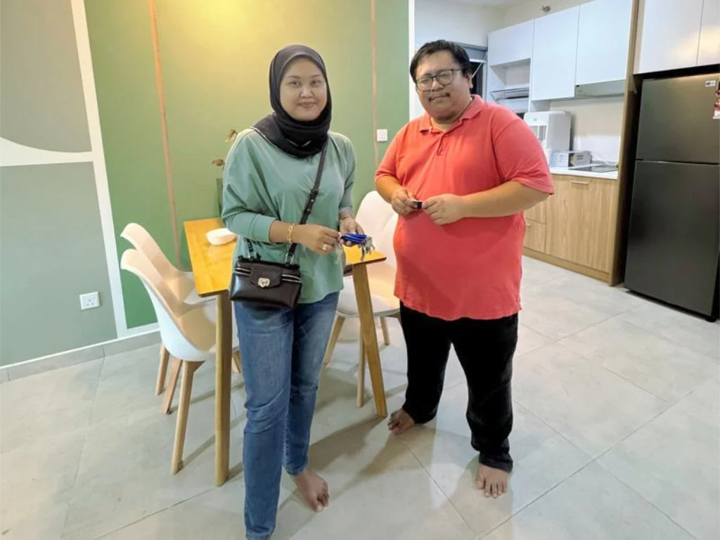 A woman and a man standing barefoot in a kitchen, holding keys, smiling at the camera.