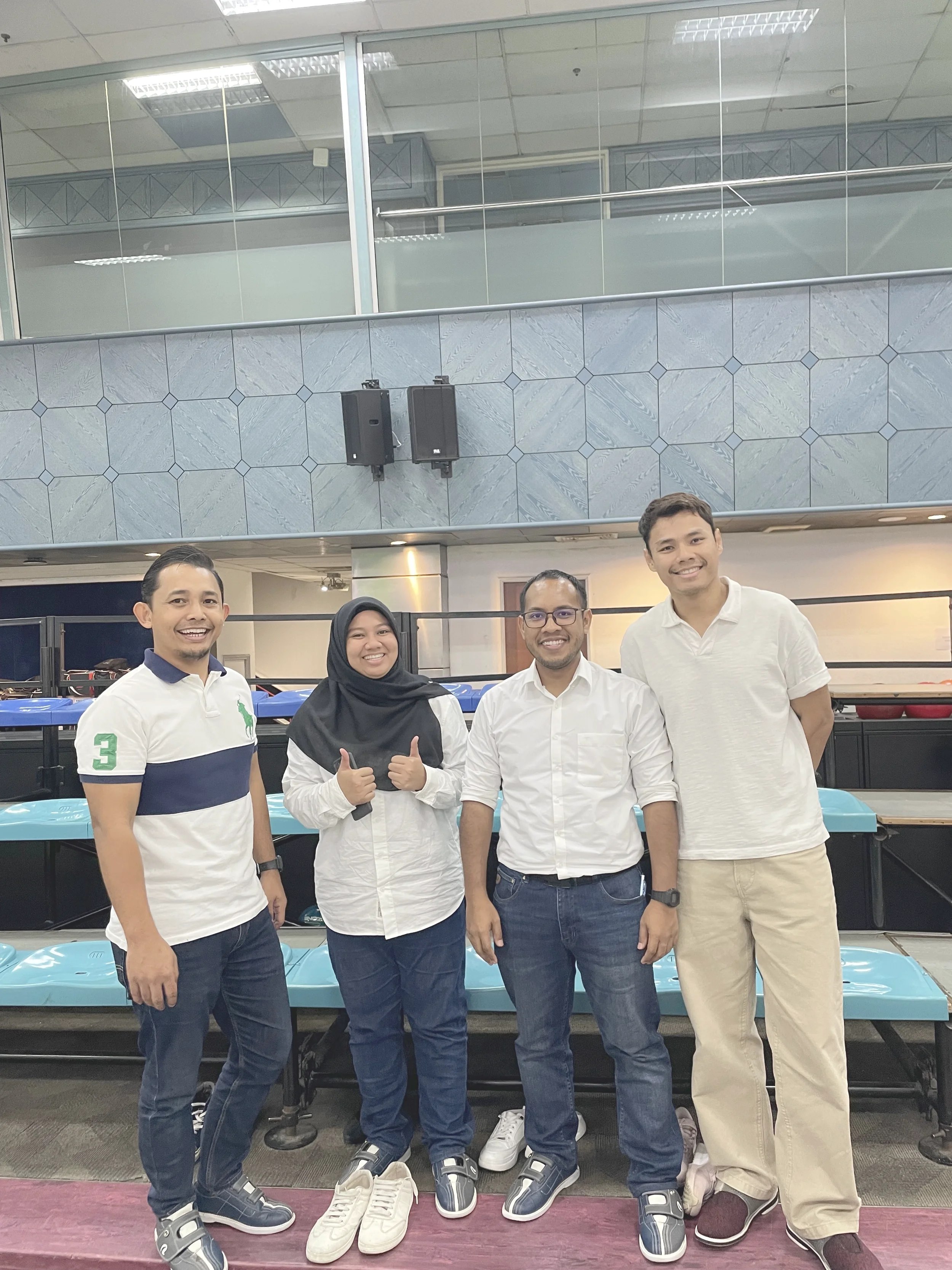 Group of five smiling people standing in front of a buffet table at an indoor event, with a tiled wall and glass railing in the background.