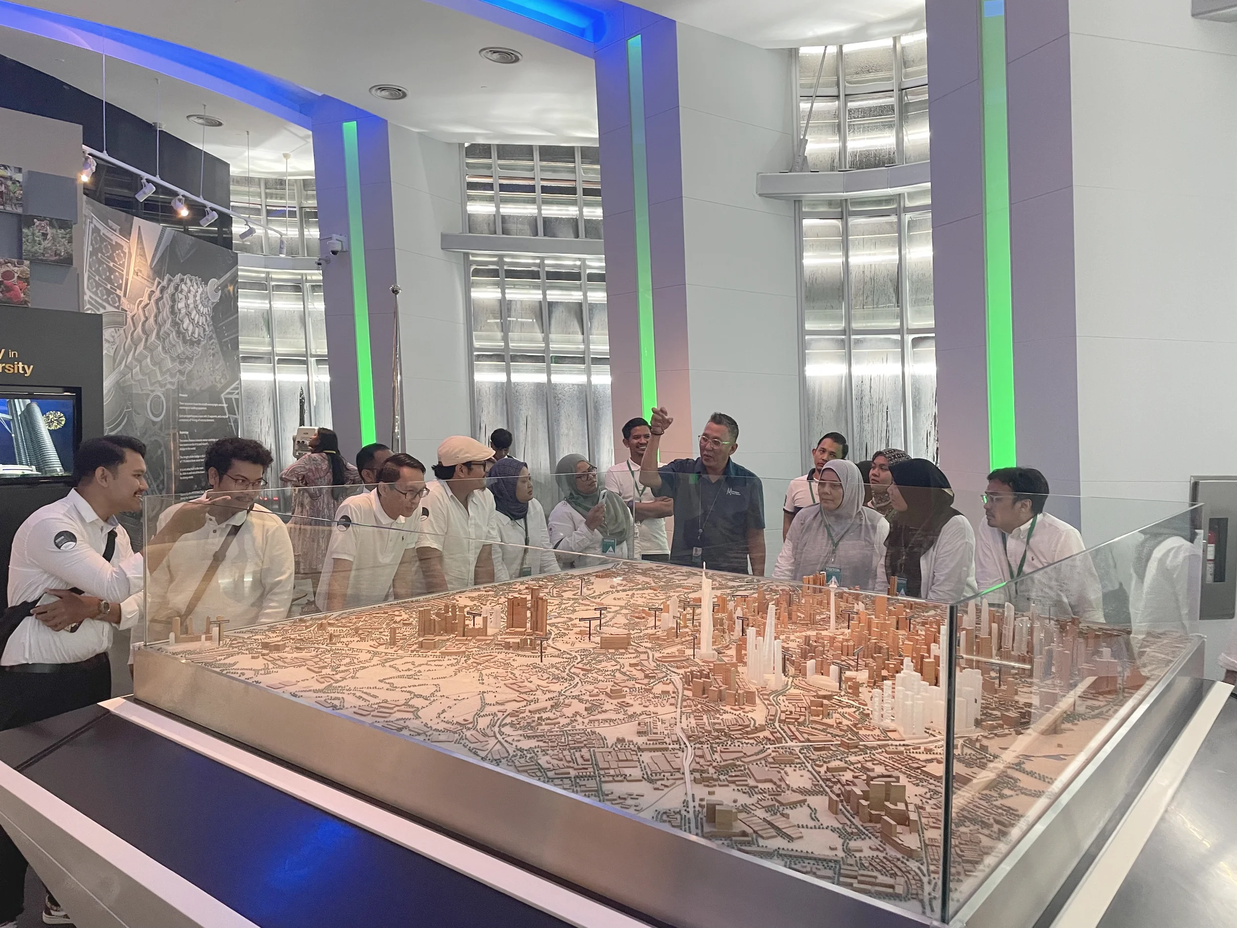 People observing a detailed architectural city model at a modern exhibition space.