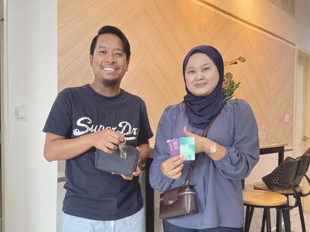 A woman wearing a hijab and a man holding a small wallet and some cards, standing inside a modern cafe or restaurant.