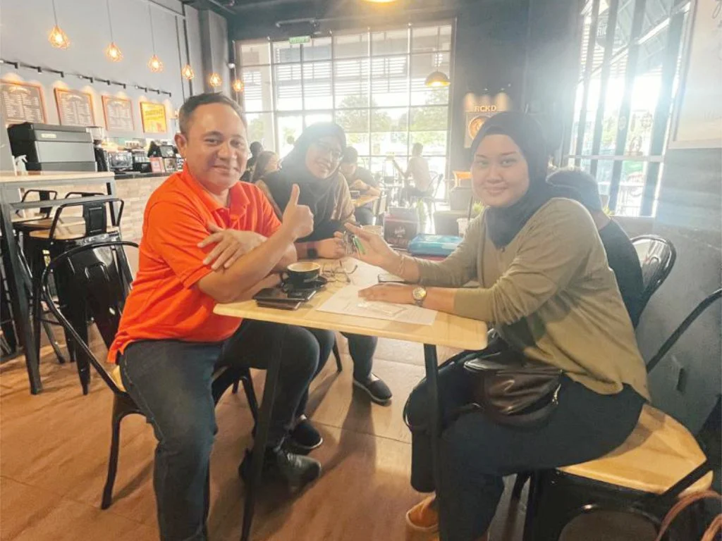 Three people sitting at a table inside a coffee shop, with two women and one man, engaging in conversation.