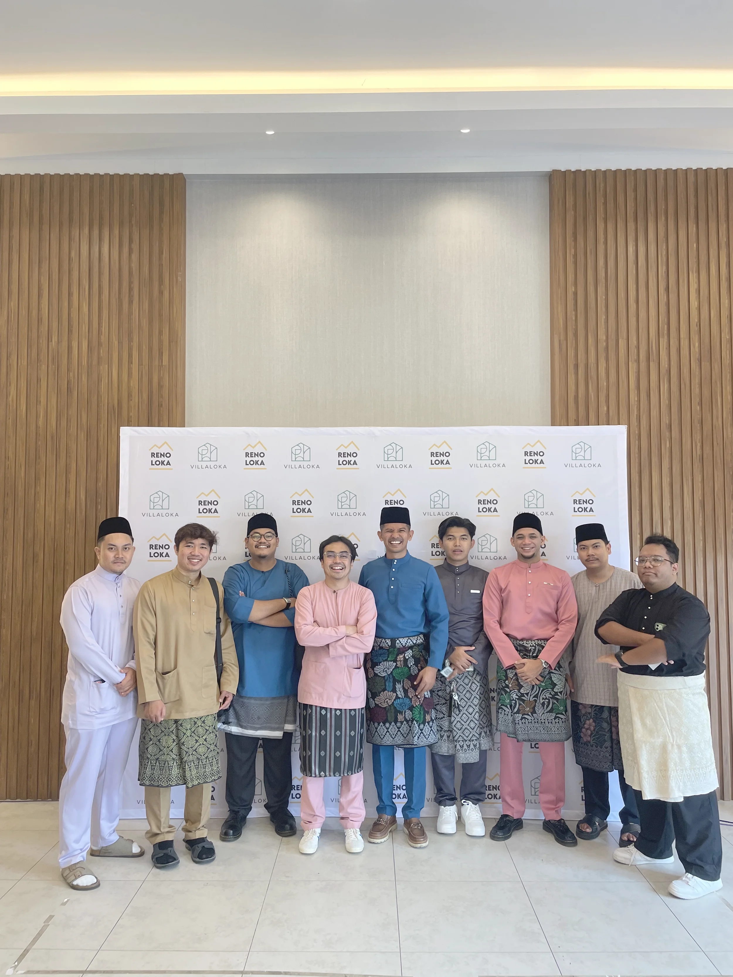 Group of men in traditional Malay attire standing in front of a backdrop with the logo 'VILLALOKA' and 'RENO LOKA', posing for a photo indoors.