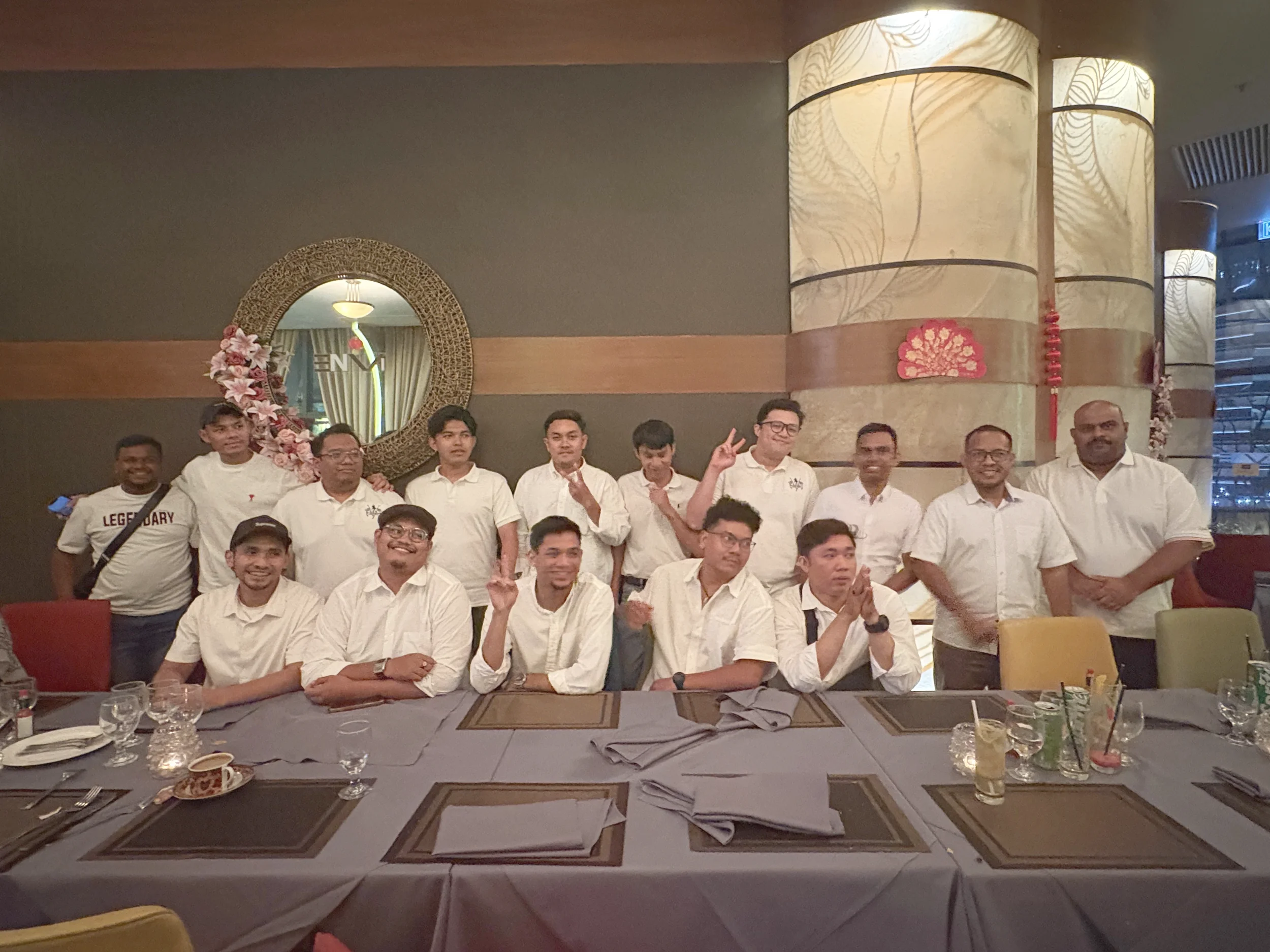 Group of people in white shirts posing for a photo in a restaurant with decorated walls and a large mirror.