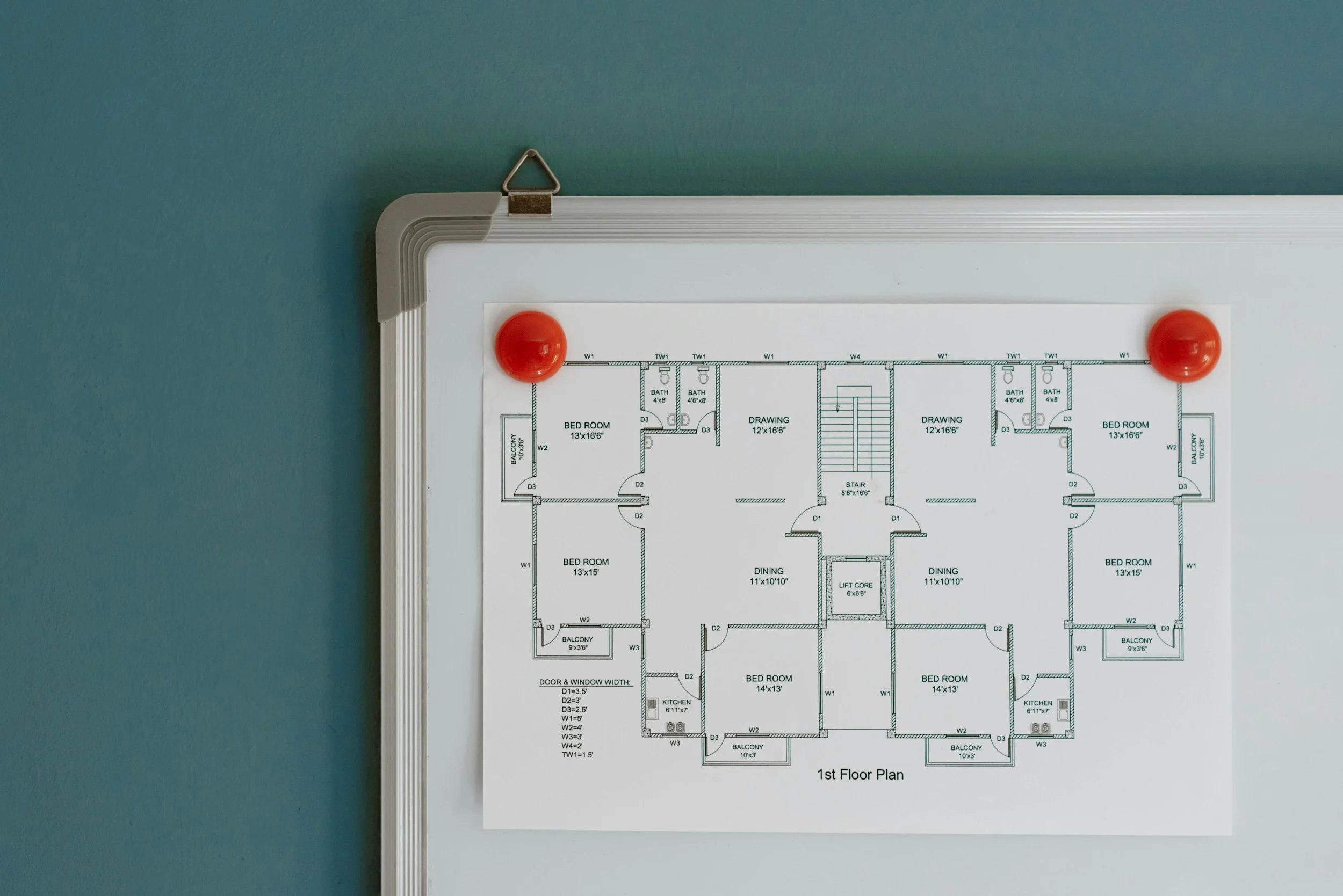 Close-up of a whiteboard with red magnets holding a detailed architectural floor plan against a teal wall.