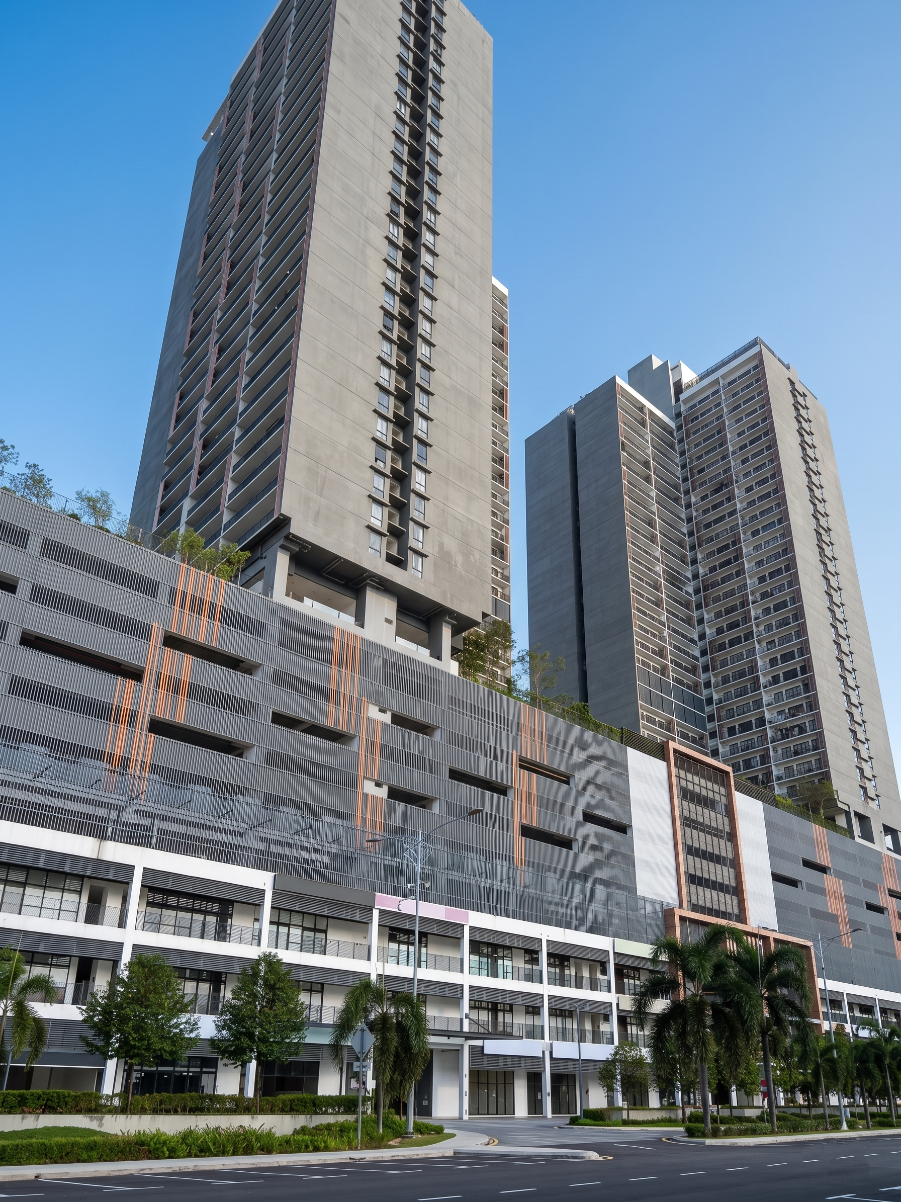 Modern high-rise buildings with glass and concrete architecture, trees, and a clear blue sky.