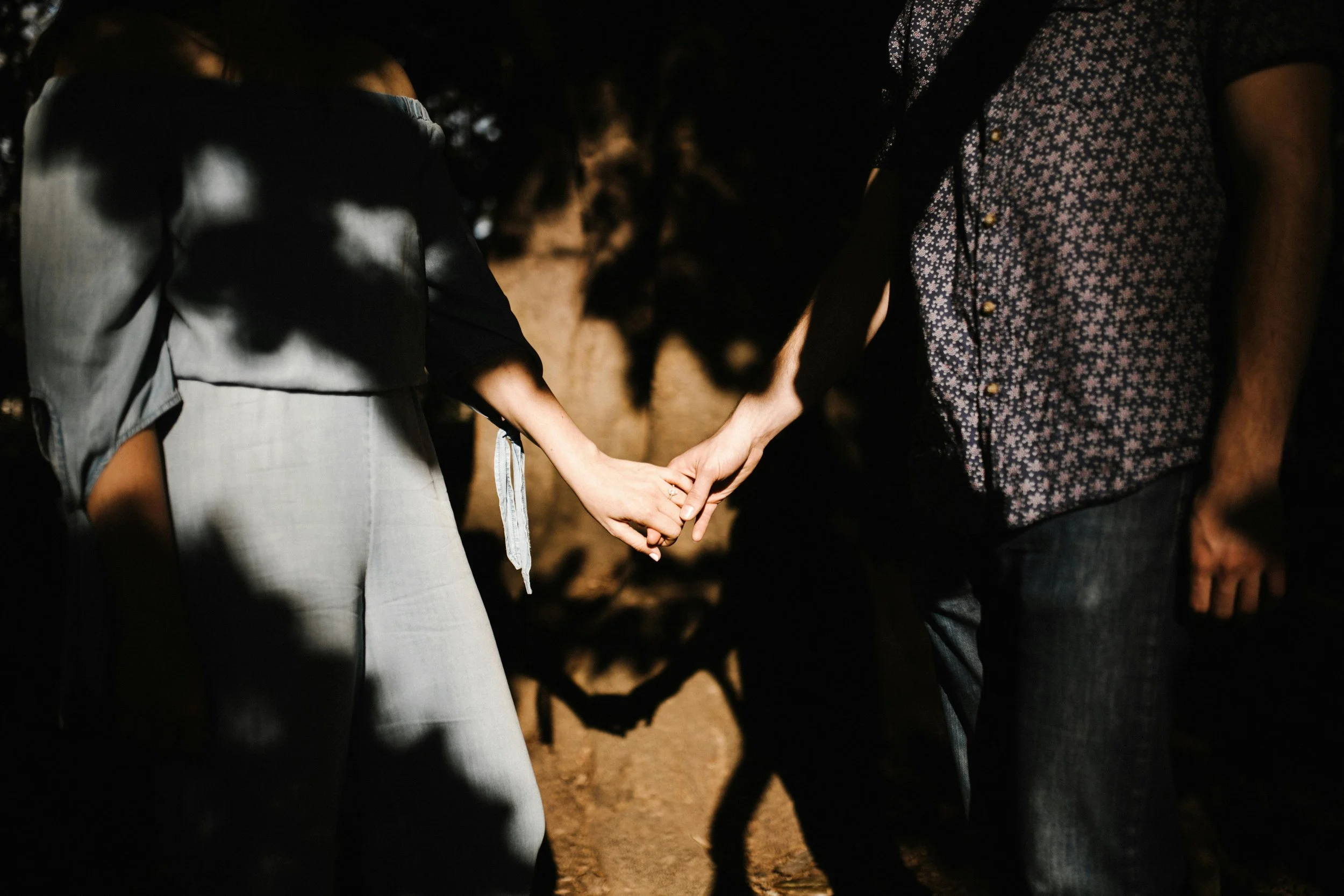 A man and a woman holding hands at night, with shadows cast on their bodies and the ground illuminated by a light source.