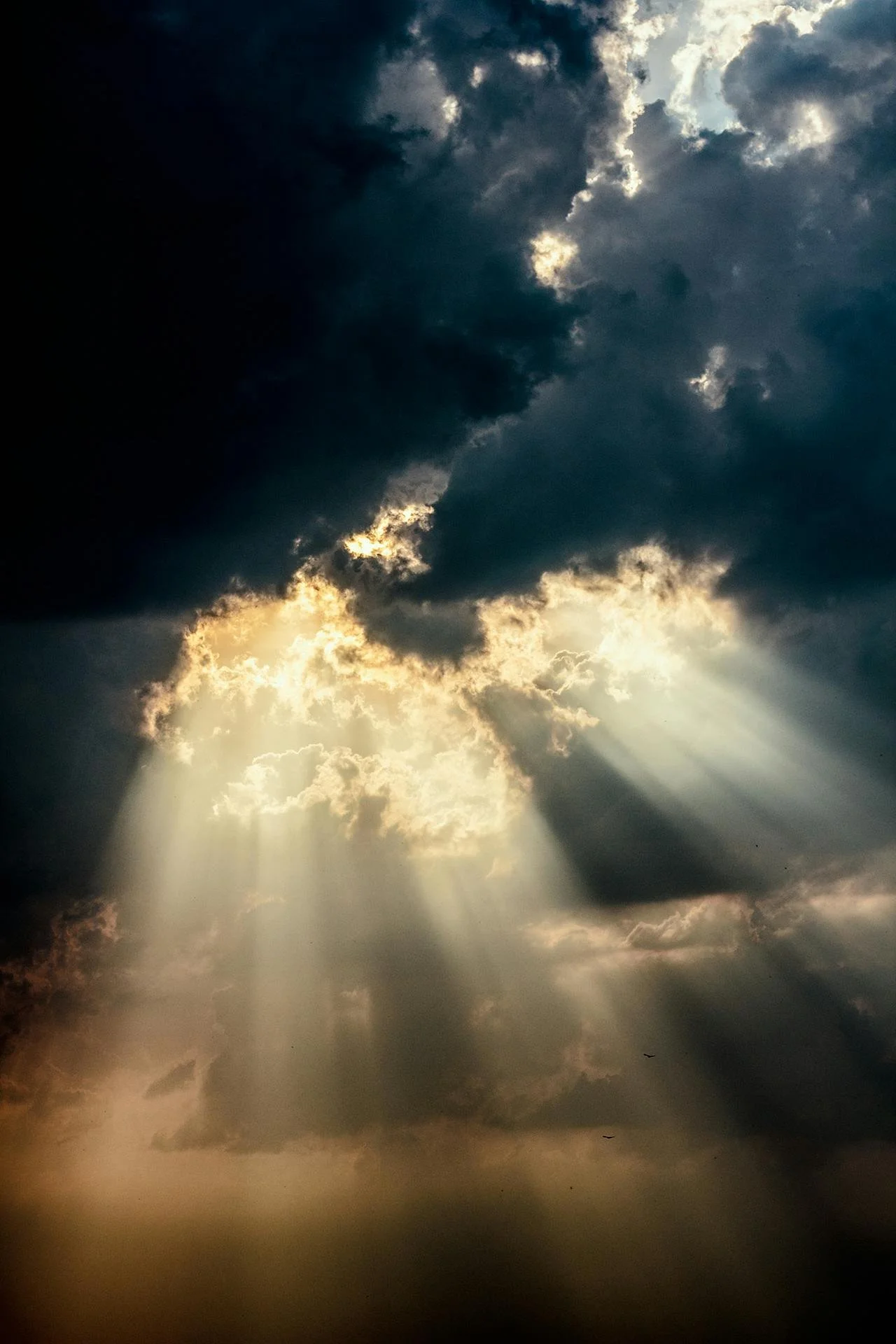 Sunlight beams breaking through dark, heavy clouds in the sky.