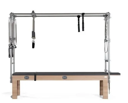 Pilates or fitness reformer machine with a padded platform, resistance straps, and a metal frame, placed on a wooden bench.