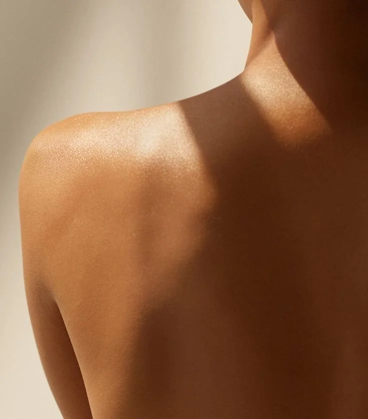 Close-up of a person's shoulder and collarbone with smooth skin, lit with soft lighting