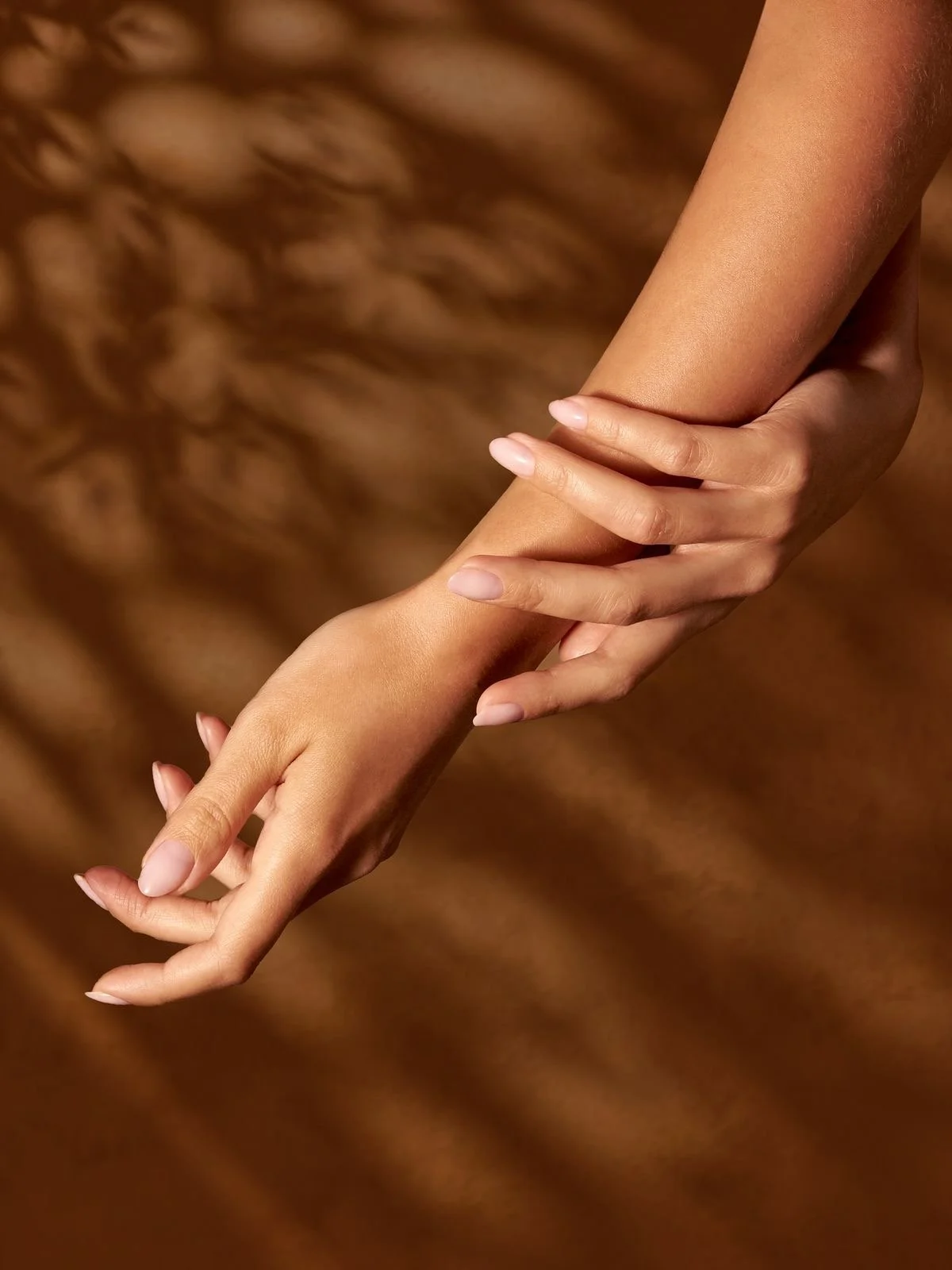Two hands, one gently grasping the other, against a brown, textured background that resembles fur or a similar material.