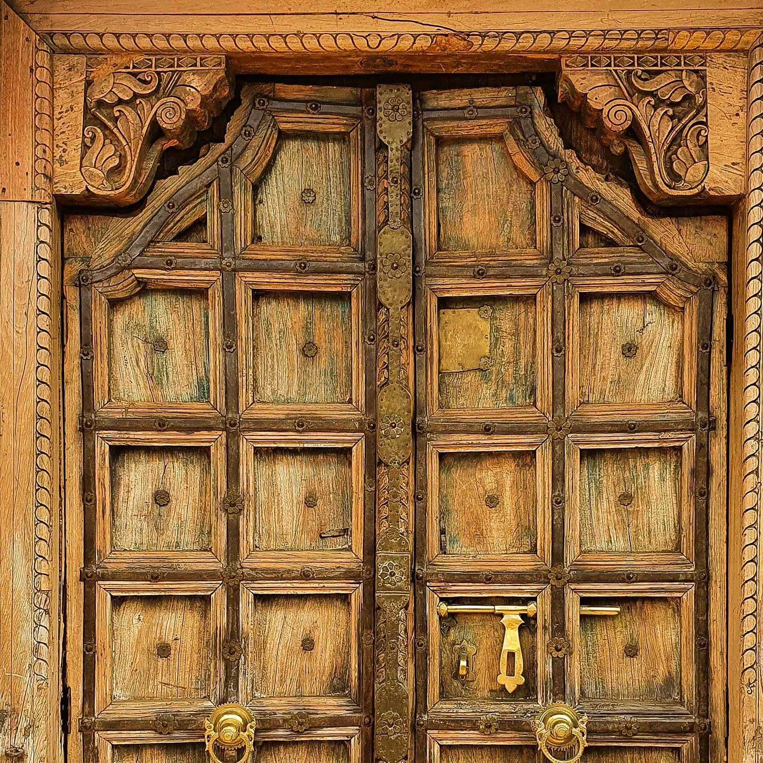 Close-up of an ornate, vintage wooden door with carved details, metal accents, and a gold door handle.