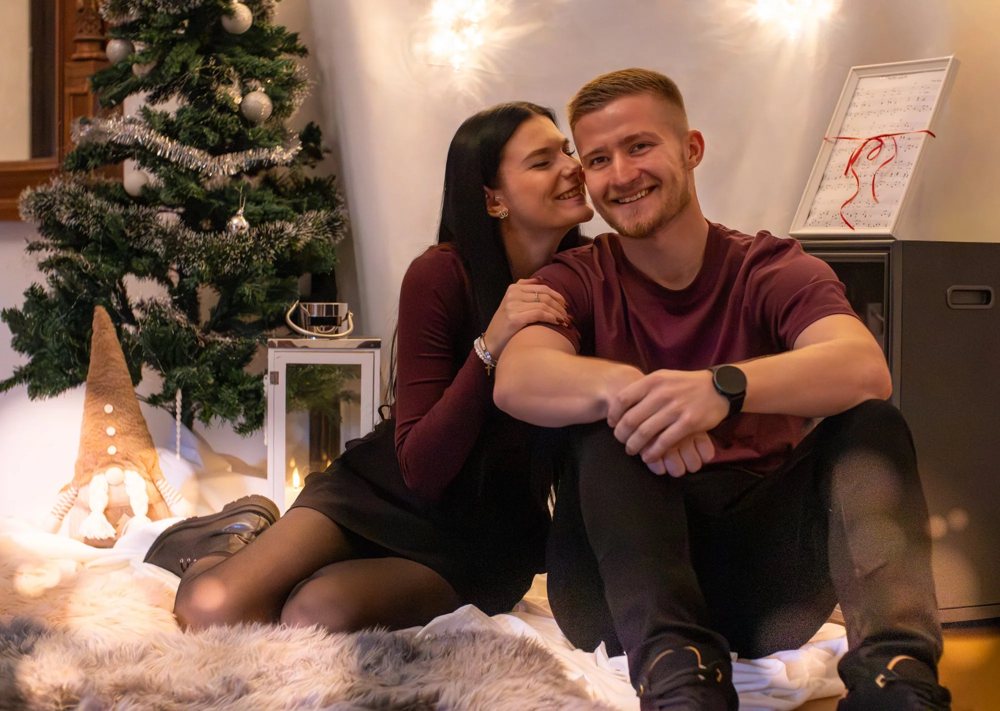 Paare sitzen zusammen im Weihnachtszimmer, umgeben von einem Weihnachtsbaum, Weihnachtsdekoration und Kunst. Sie sind glücklich und lachen, während sie die festliche Atmosphäre genießen.