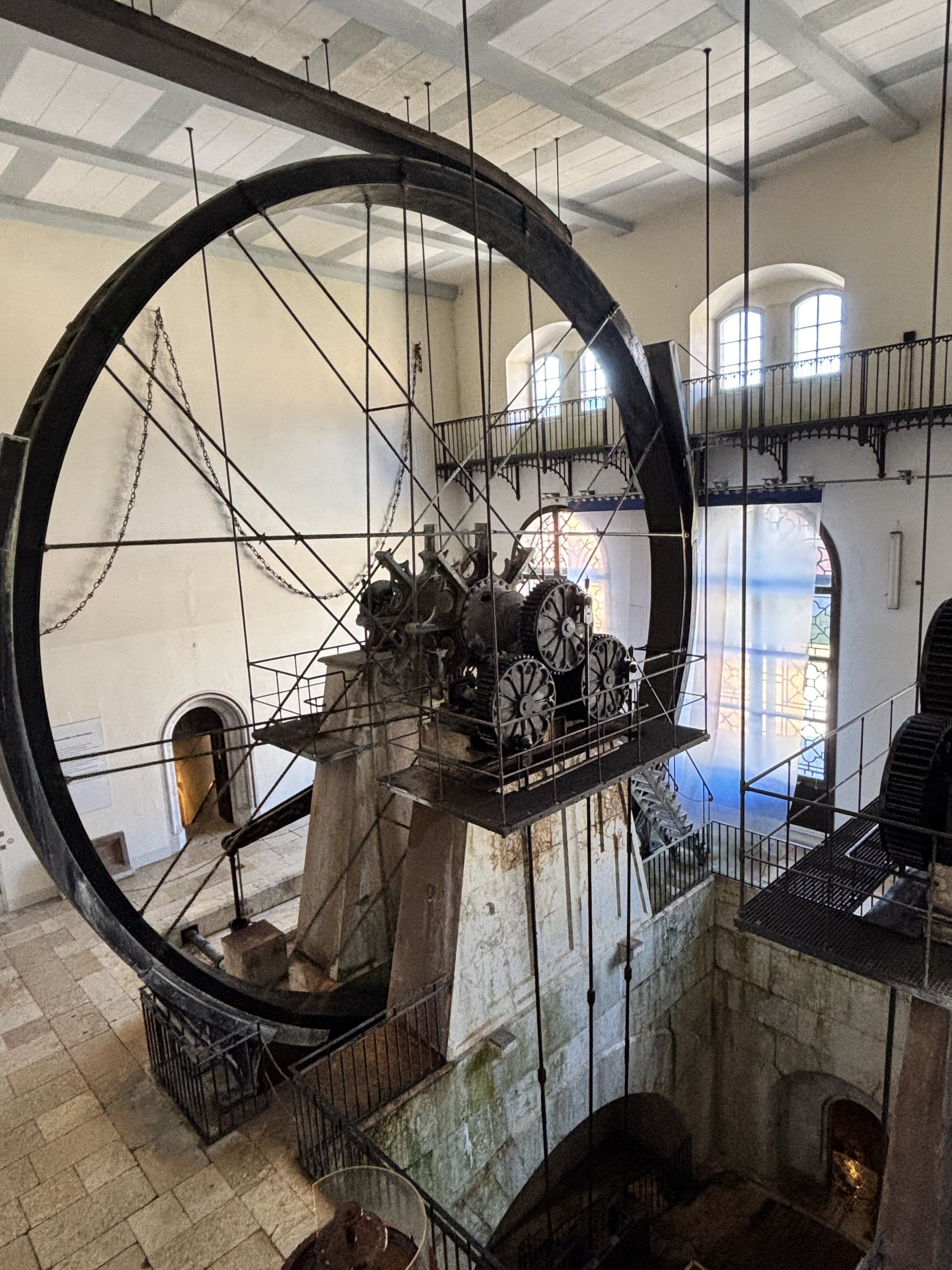 Historische Turbine im Museum, mit sichtbaren Zahnrädern und großer Metallkonstruktion vor hellem Innenraum mit Fenstern.