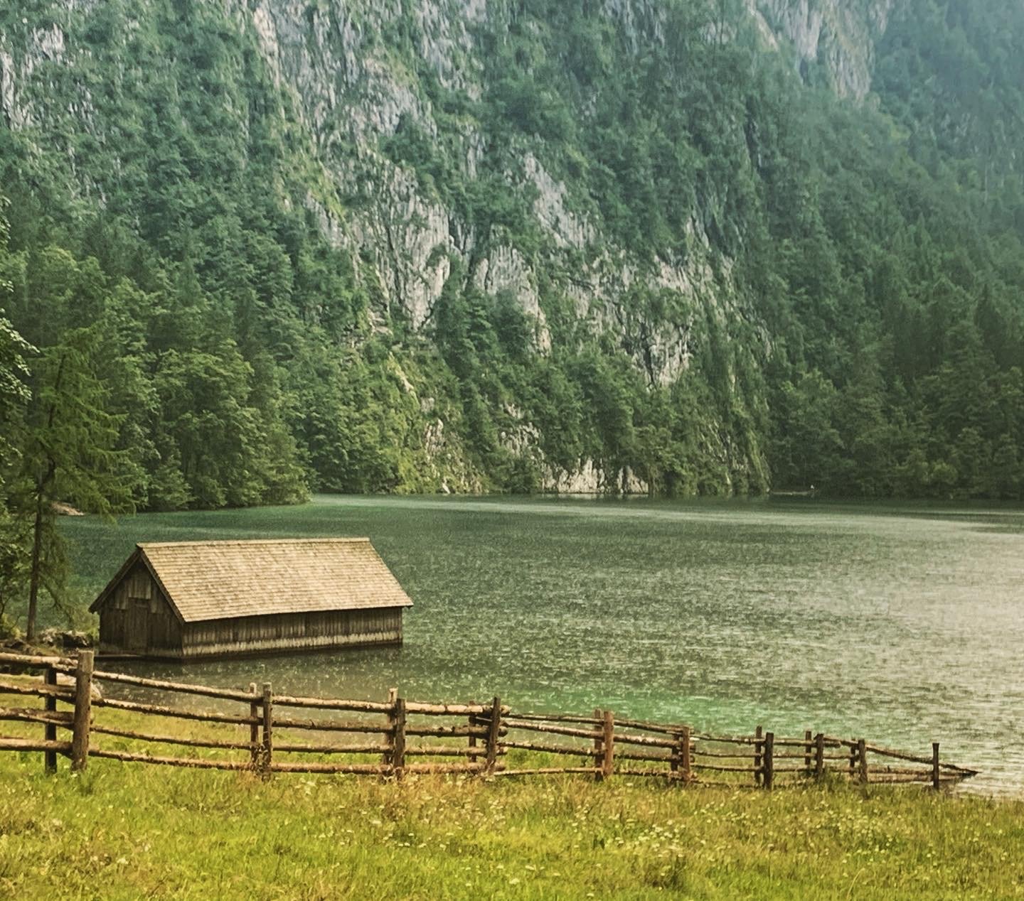 Hütten am See vor steileren, bewaldeten Bergen.